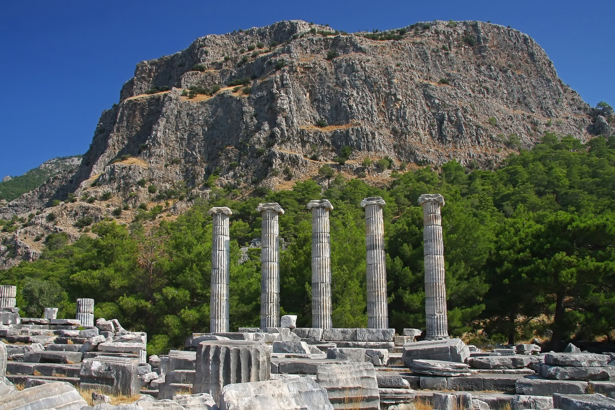Ancient ruins of Priene with columns and stone blocks on mountainous terrain