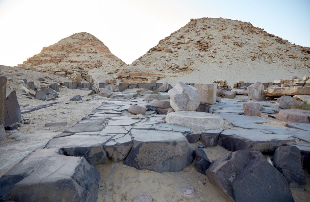 Stone pavement and scattered granite blocks with ruined pyramids in the Abusir Pyramids Complex, Cairo
