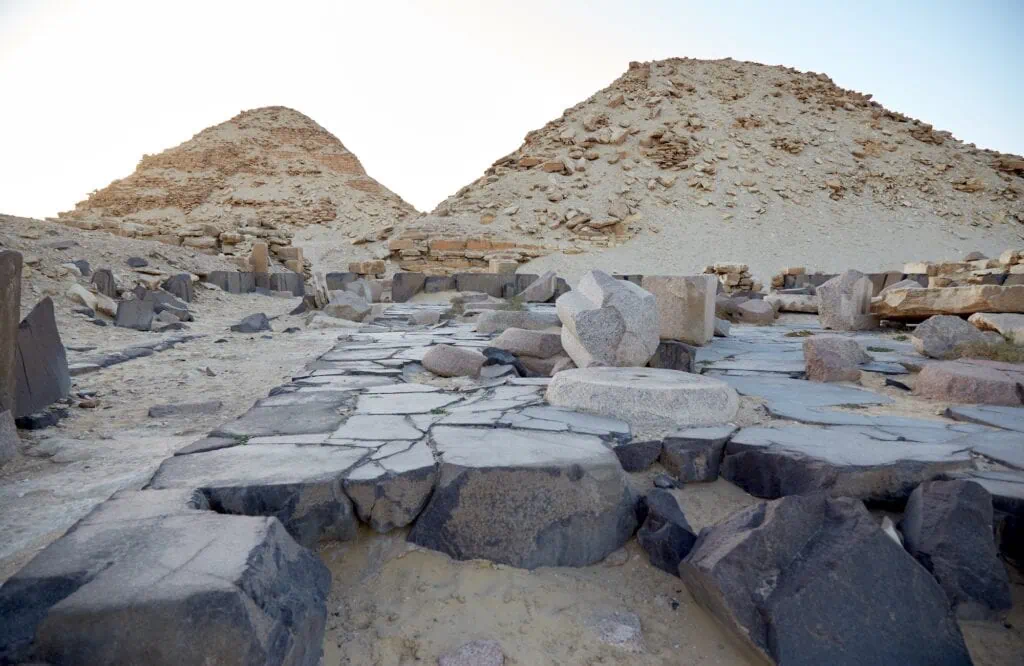 Stone pavement and scattered granite blocks with ruined pyramids in the Abusir Pyramids Complex, Cairo