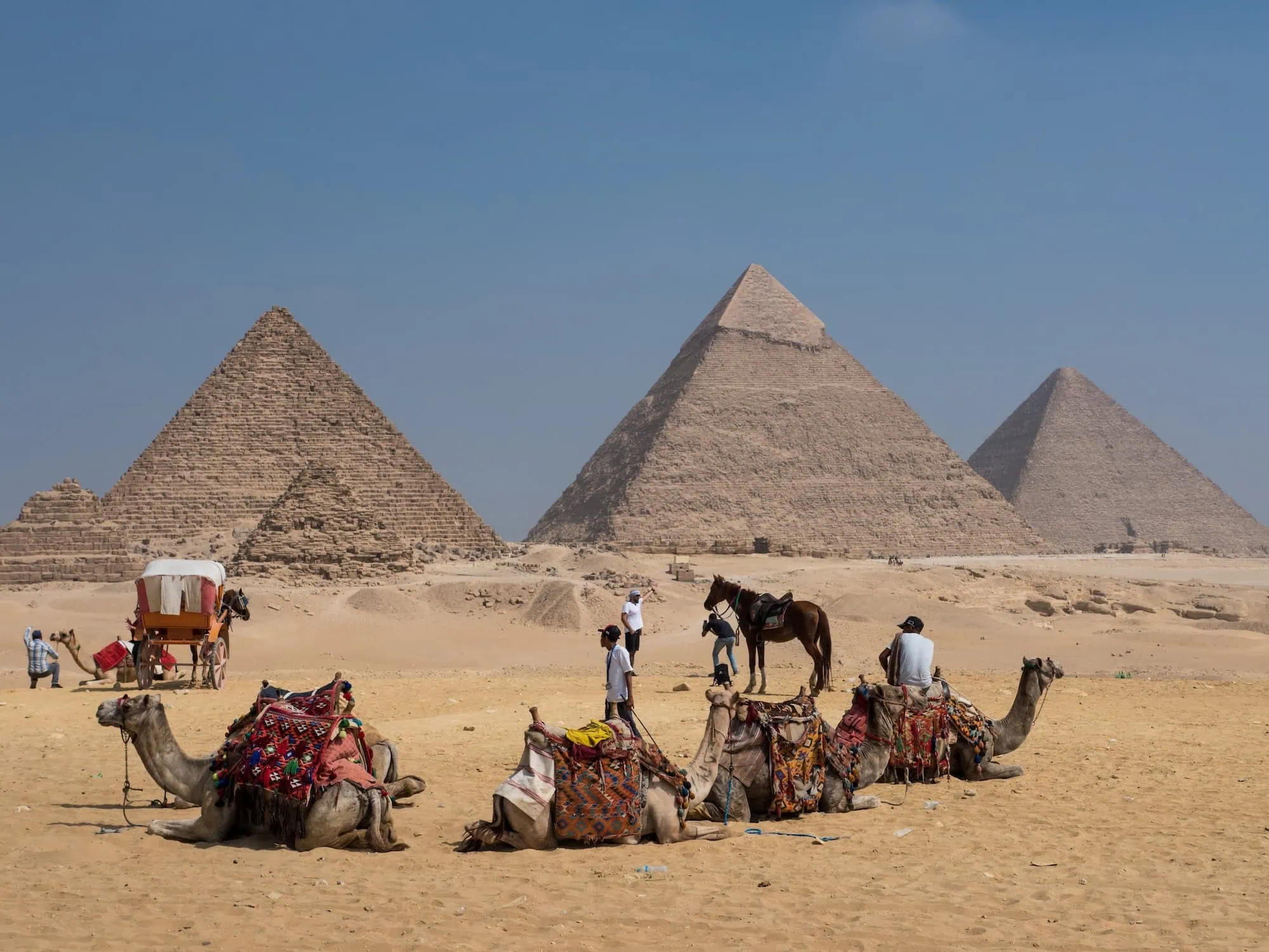 Tourists on camels and horses with local guides at the Great Pyramids of Giza