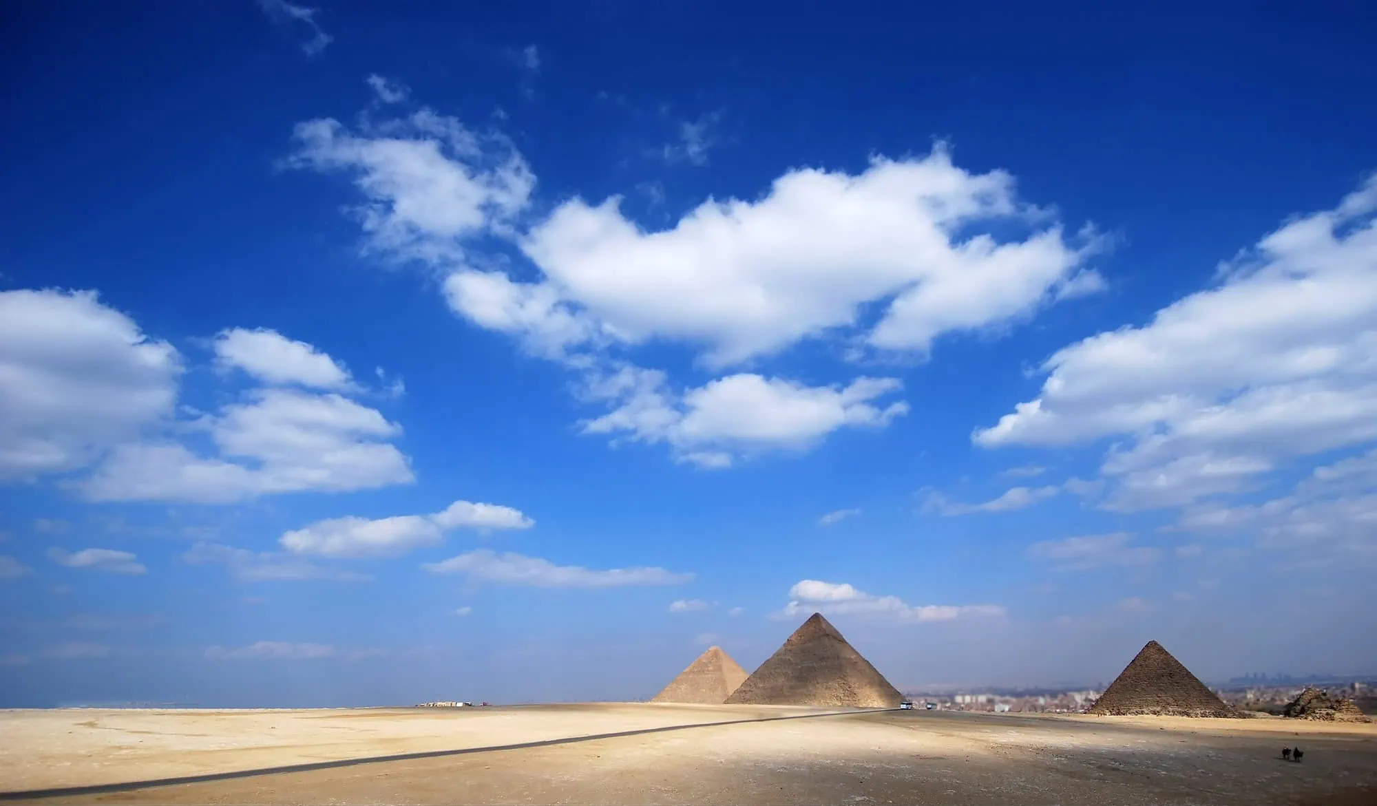 Panoramic view of the three famous pyramids of Giza against a blue sky with white clouds