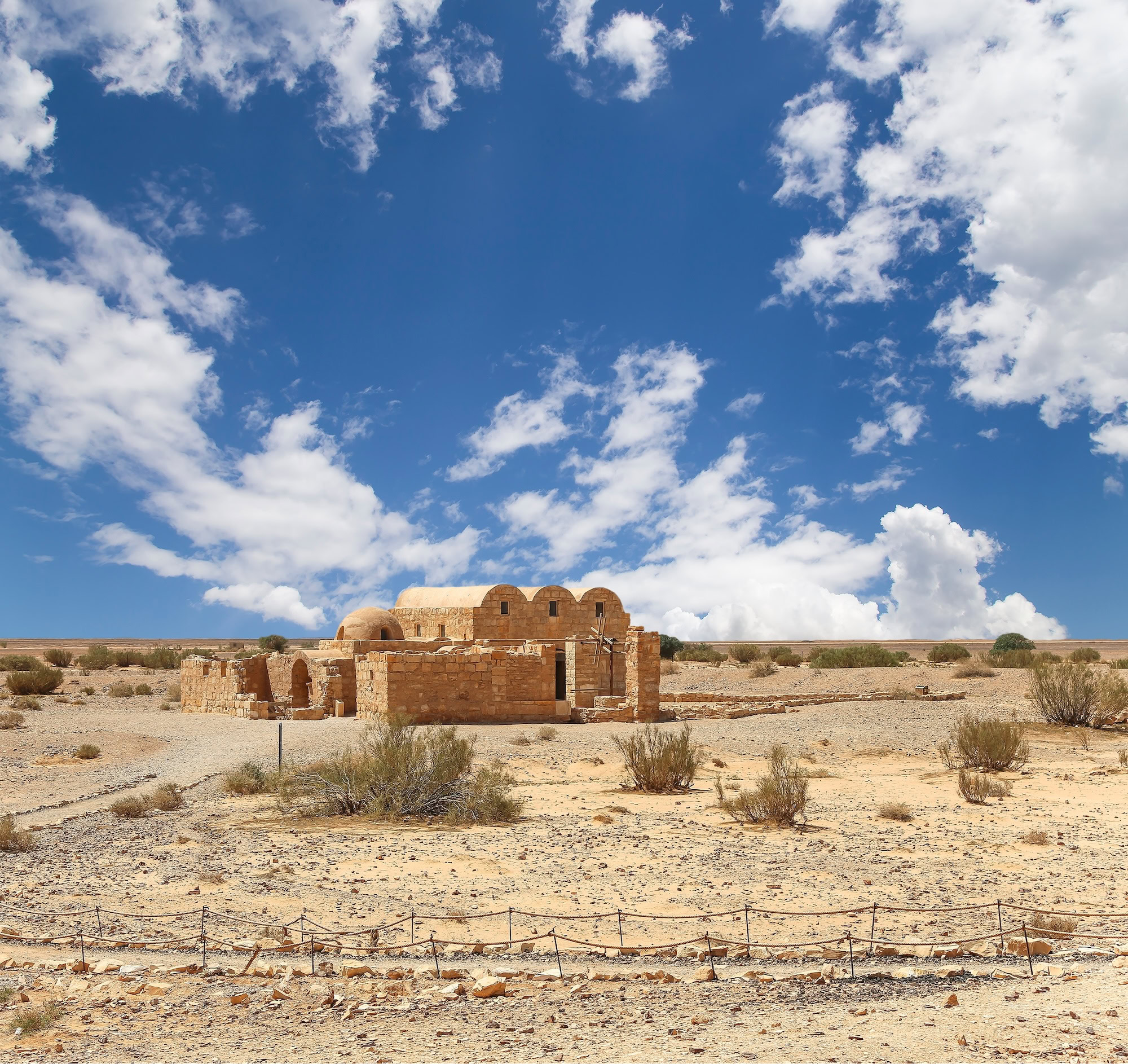 Ancient Qasr Amra bathhouse ruins with stone arches and protective fencing in Jordanian desert