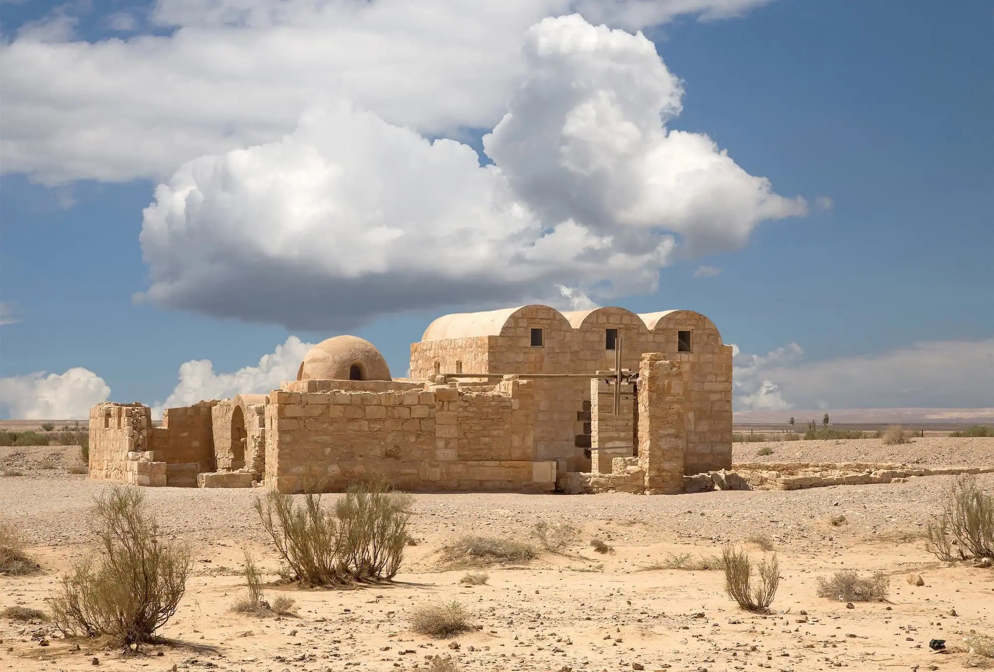 Ancient Qasr Amra desert castle showing three-arched facade and dome in Jordan desert
