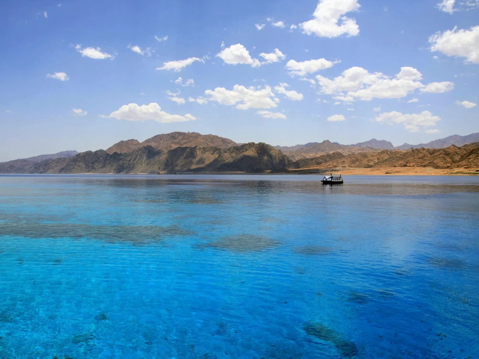Crystal clear Red Sea waters with mountains and boat showing excellent underwater visibility