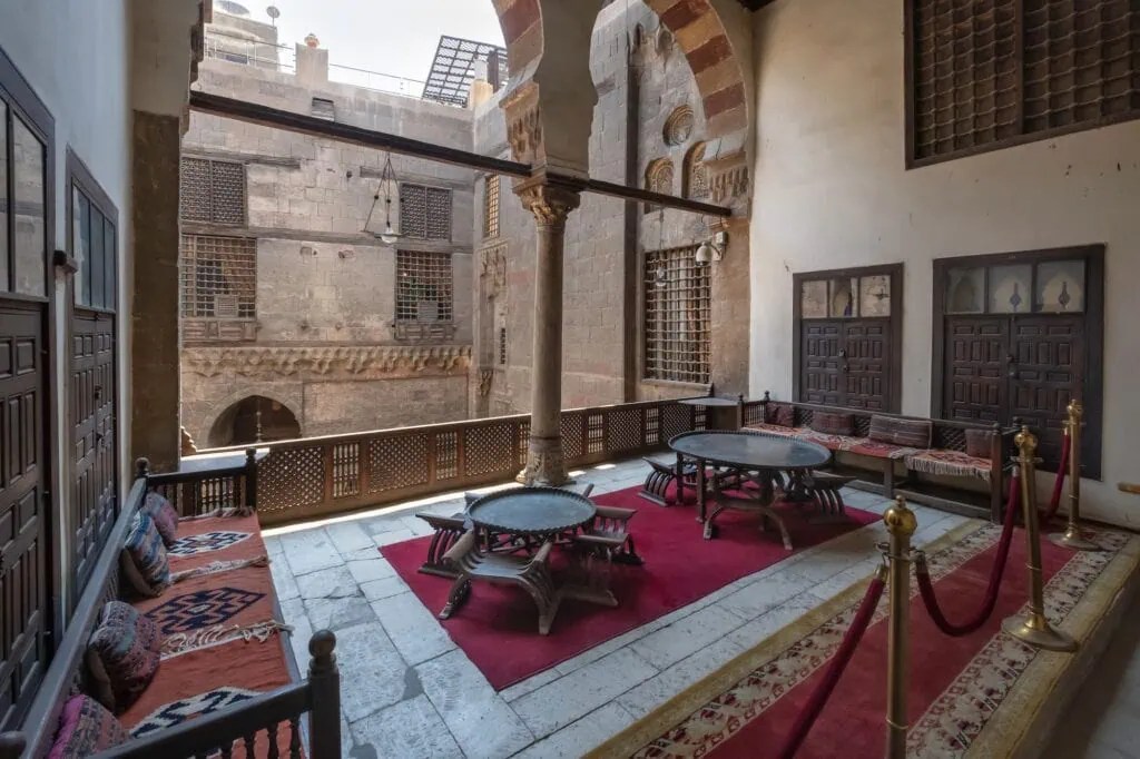 A richly decorated interior terrace with carved wooden screens, patterned tiles, columns, and traditional furnishings at the Gayer-Anderson Museum, Cairo