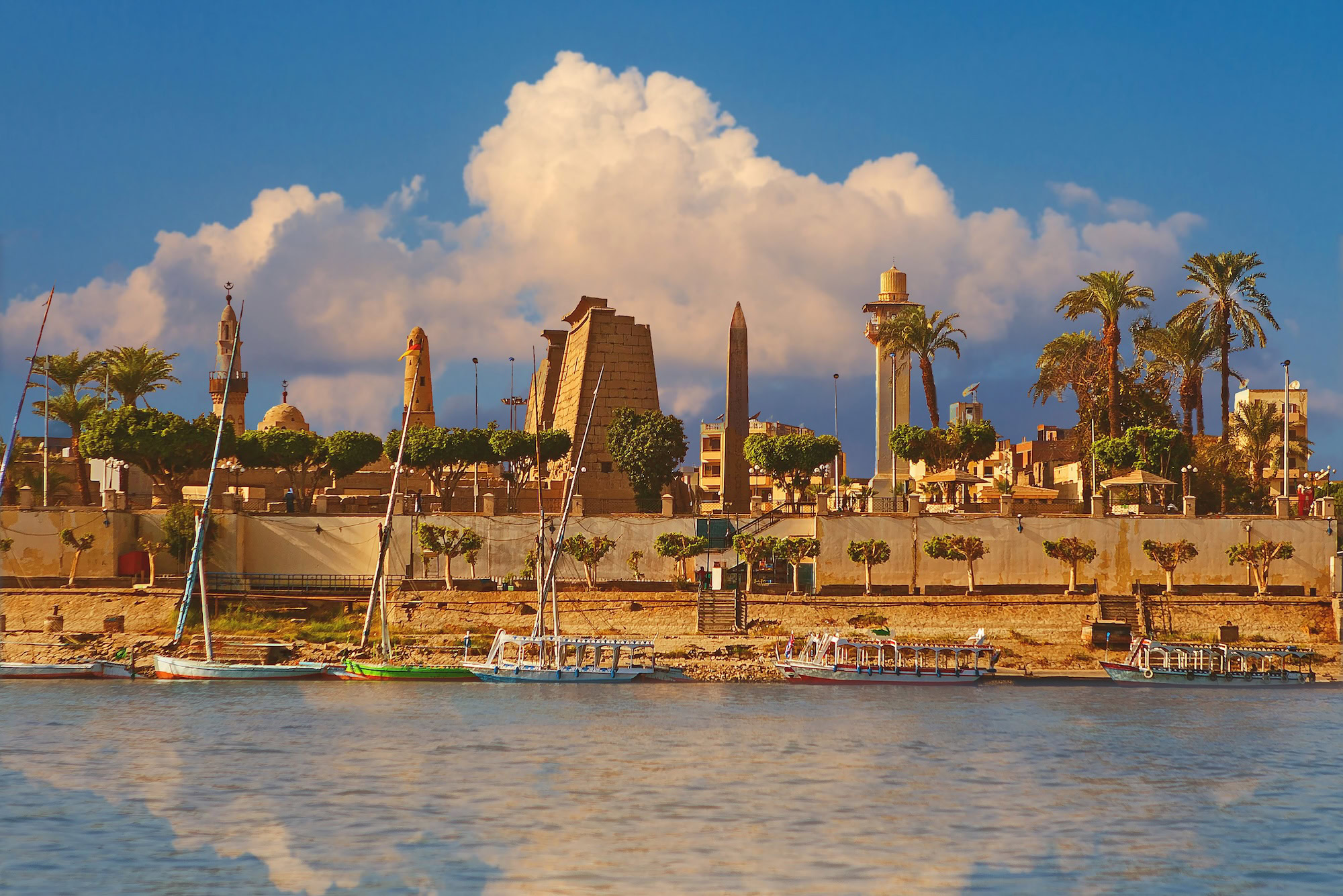Luxor Temple viewed from Nile River with traditional felucca sailboats in foreground
