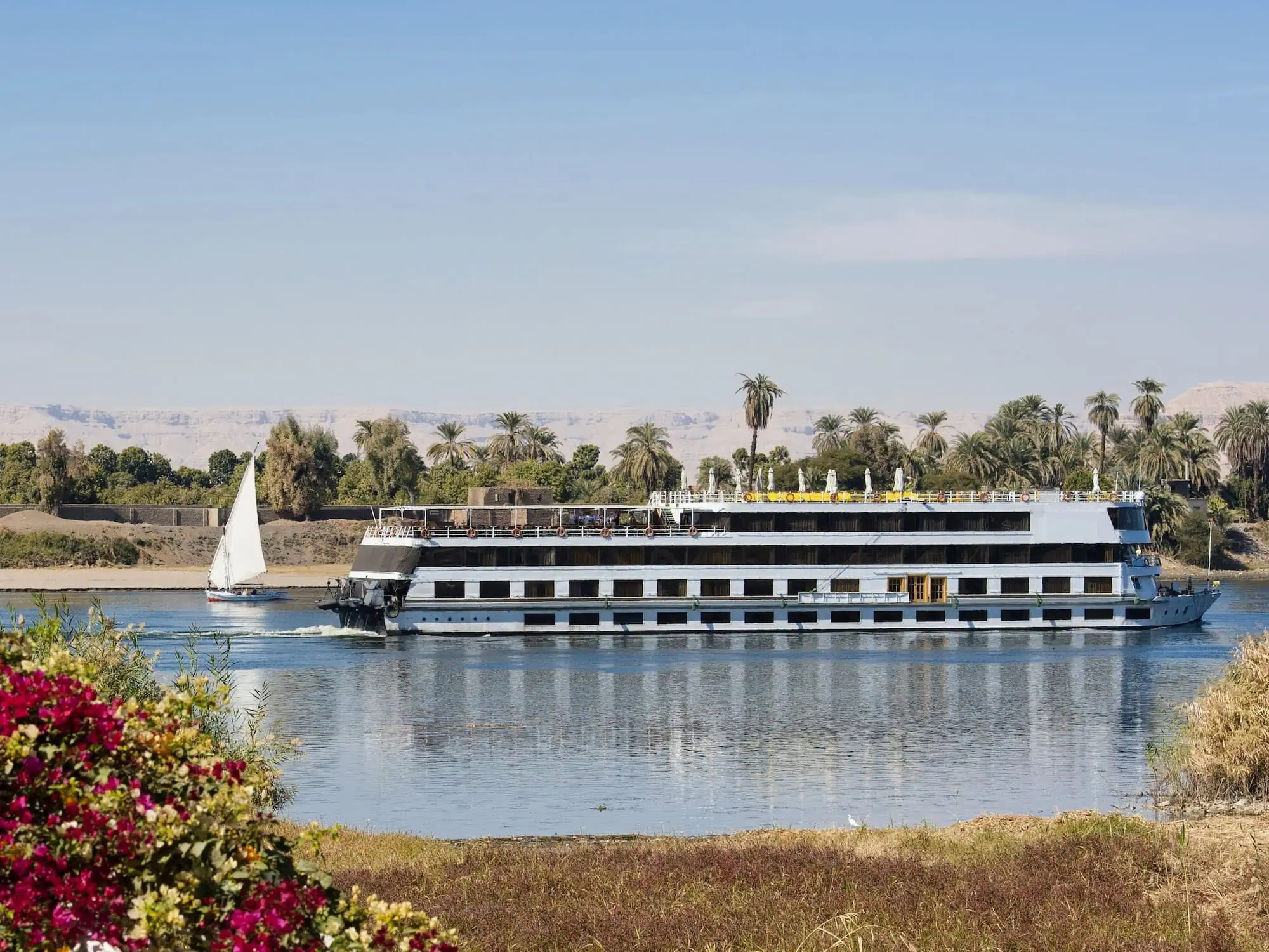 Luxury river cruise boat sailing on the Nile River with traditional felucca boat nearby