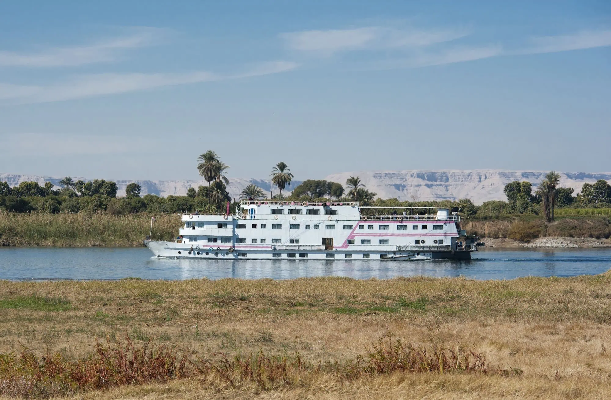 White river cruise ship sailing down the Nile River with desert landscape and palm trees