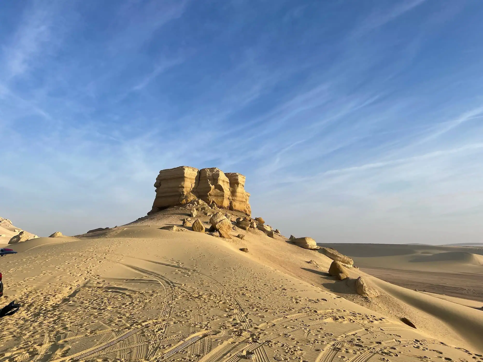 White limestone rock formations in Egypt's White Desert with sand dunes and tire tracks