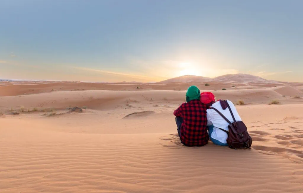 Couple sitting on sand dunes watching sunset colors at Sahara Desert in Merzouga