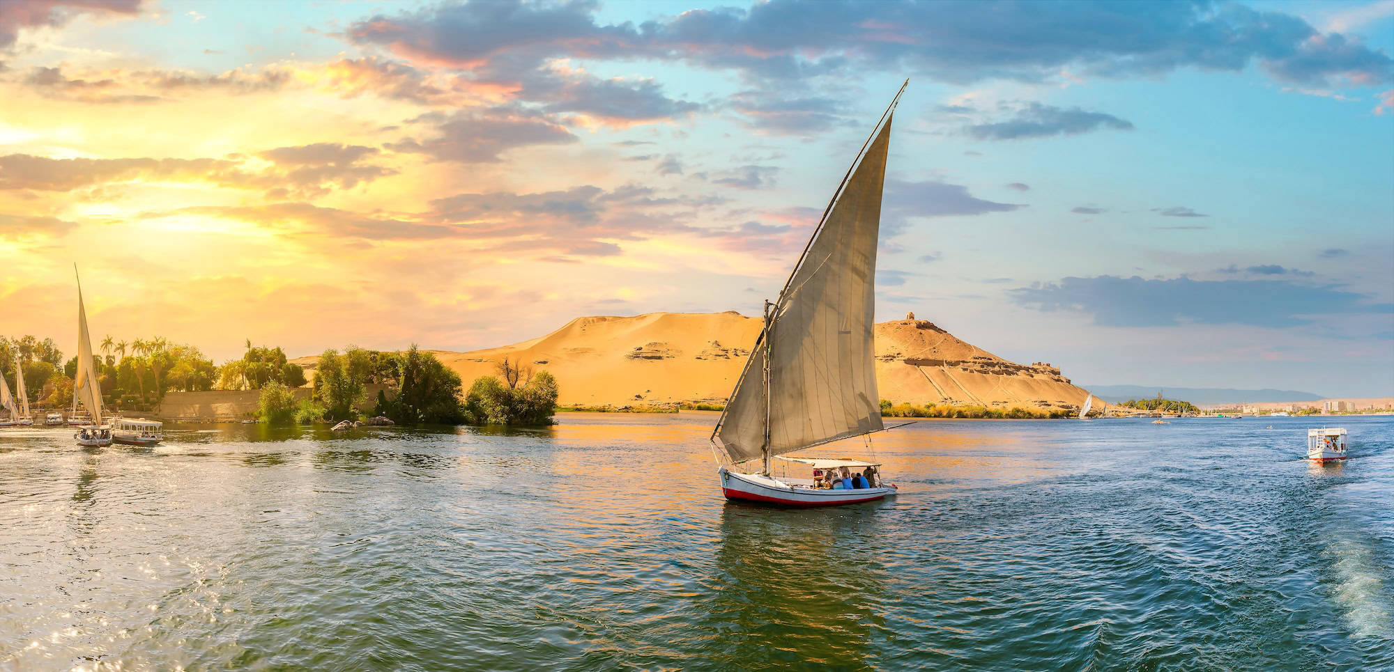 Felucca sailboat on Nile River with sand dunes and palm trees in Aswan, Egypt