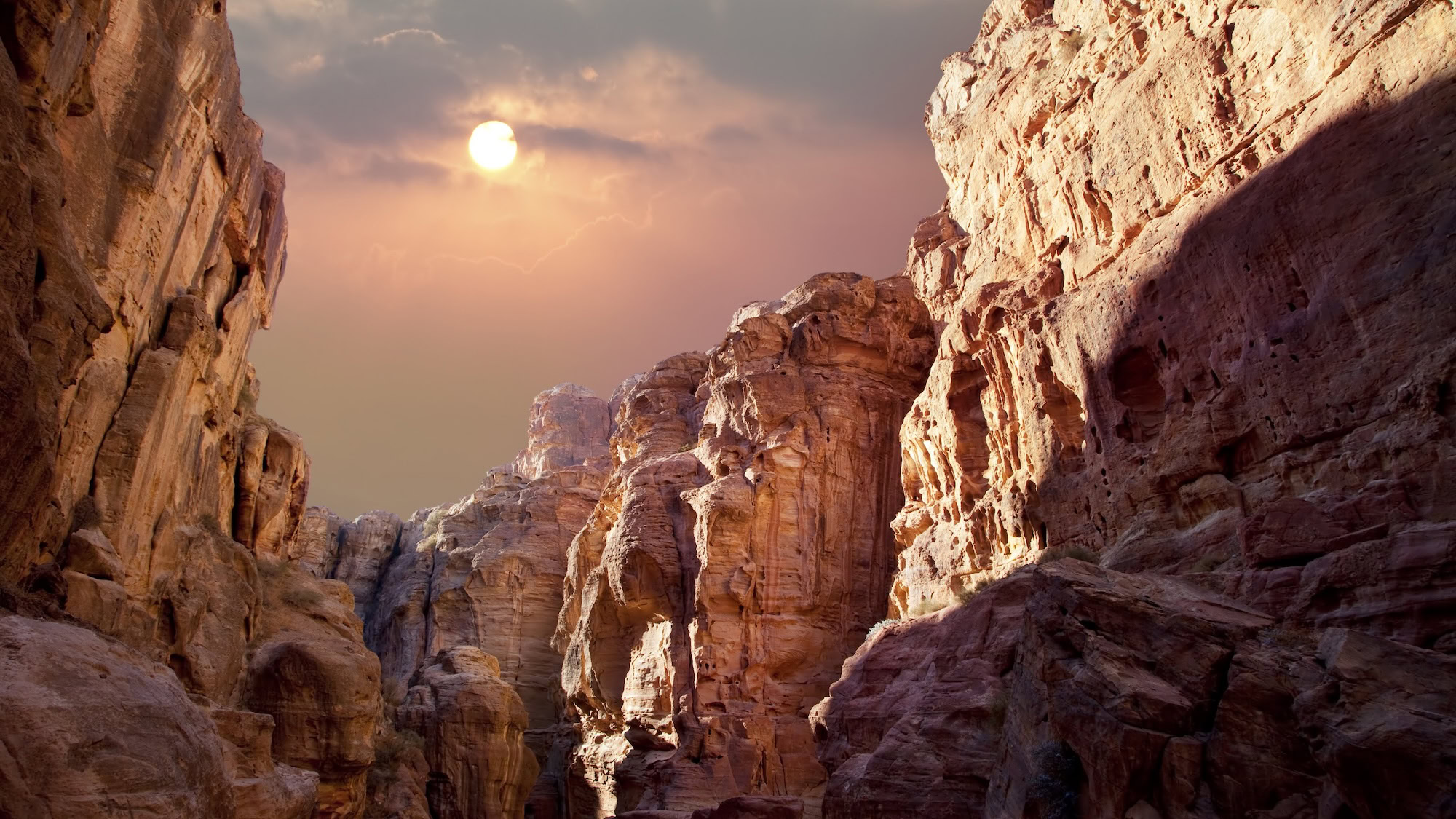 Petra's pink sandstone canyon with sunlight streaming through creating dramatic sunset lighting