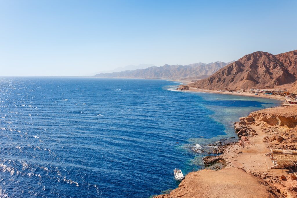 Rocky sea coast with clear blue water and divers entering the Blue Hole along the Red Sea shoreline, Dahab