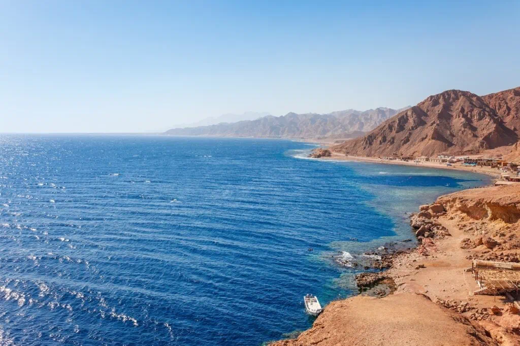 Rocky sea coast with clear blue water and divers entering the Blue Hole along the Red Sea shoreline, Dahab