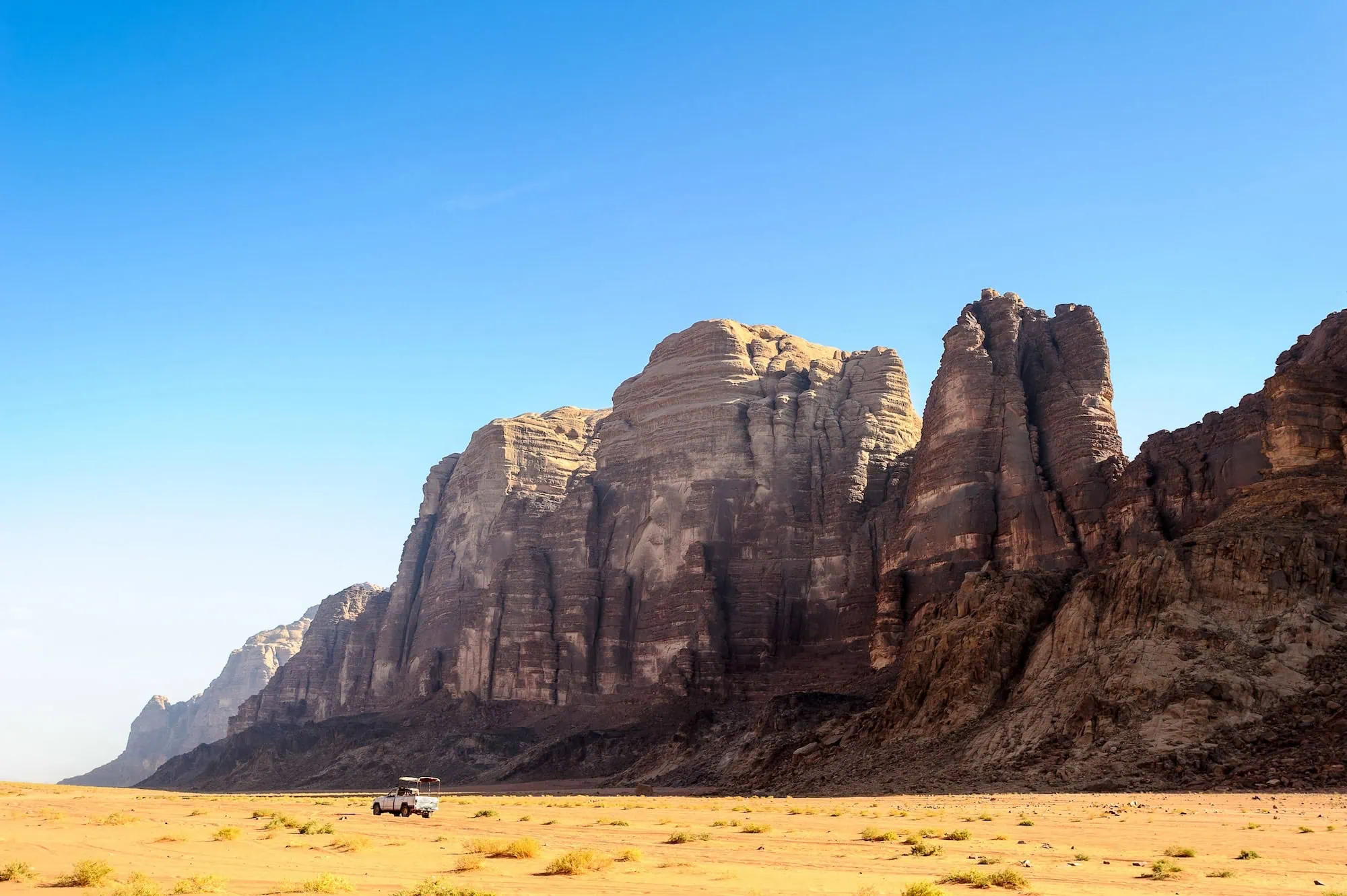 Dramatic sandstone cliffs and rock formations rising from golden desert floor in Wadi Rum, Jordan