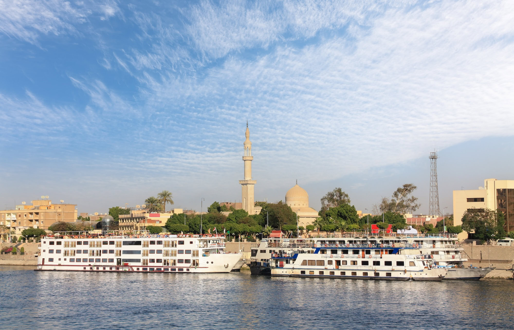 Several cruise ships lie on the banks of the Nile in the Upper Egyptian city of Luxor. In the background is the city with buildings and a minaret