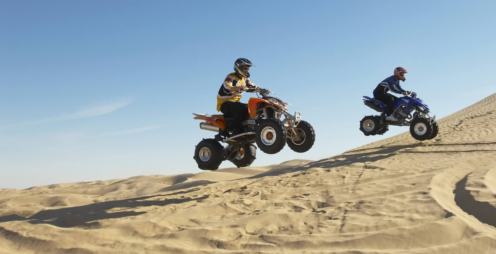 Side view of two men doing wheelies on quad bikes in the desert 1905x976 crop 50 41