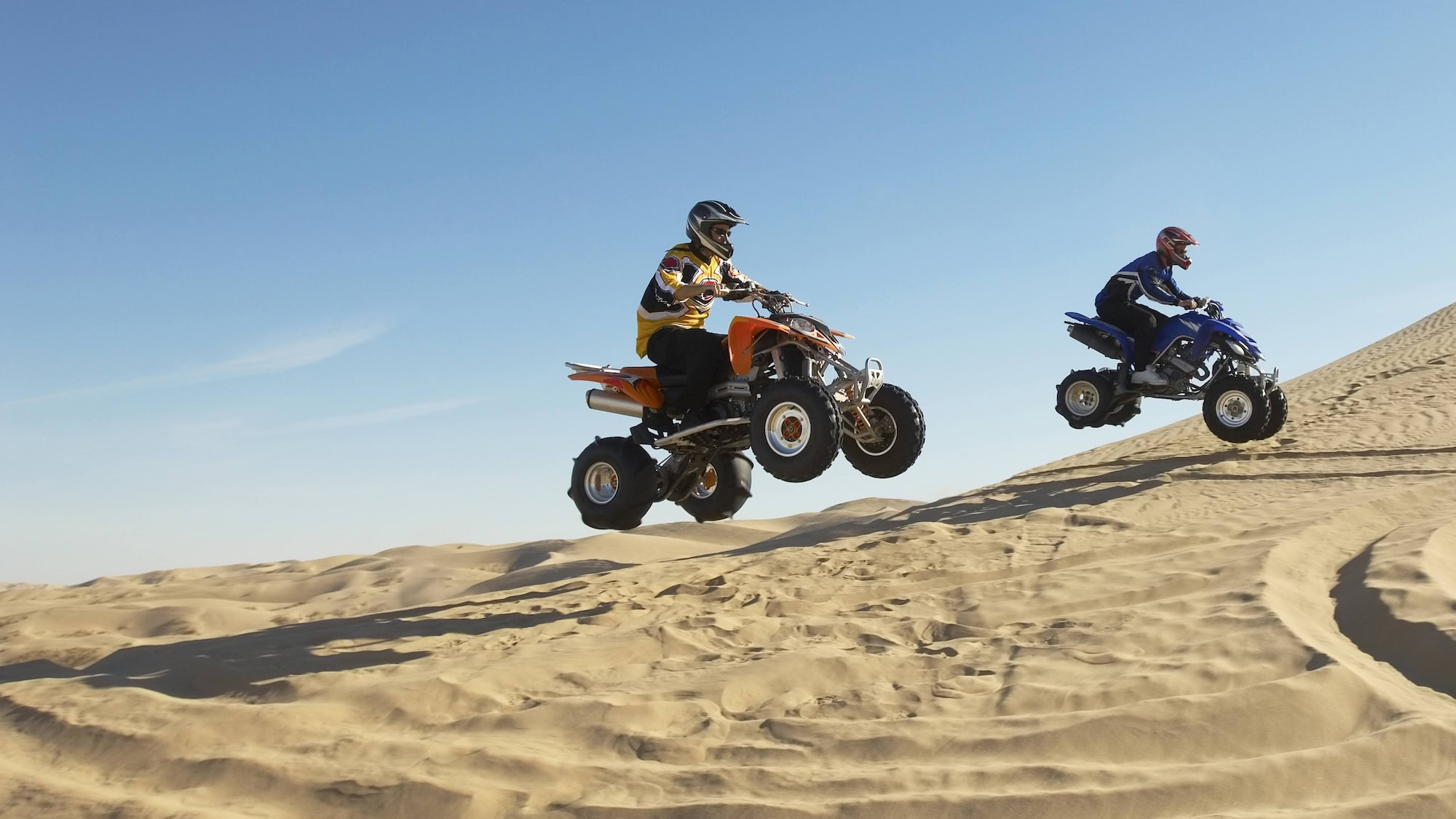 Side view of two men doing wheelies on quad bikes in the desert