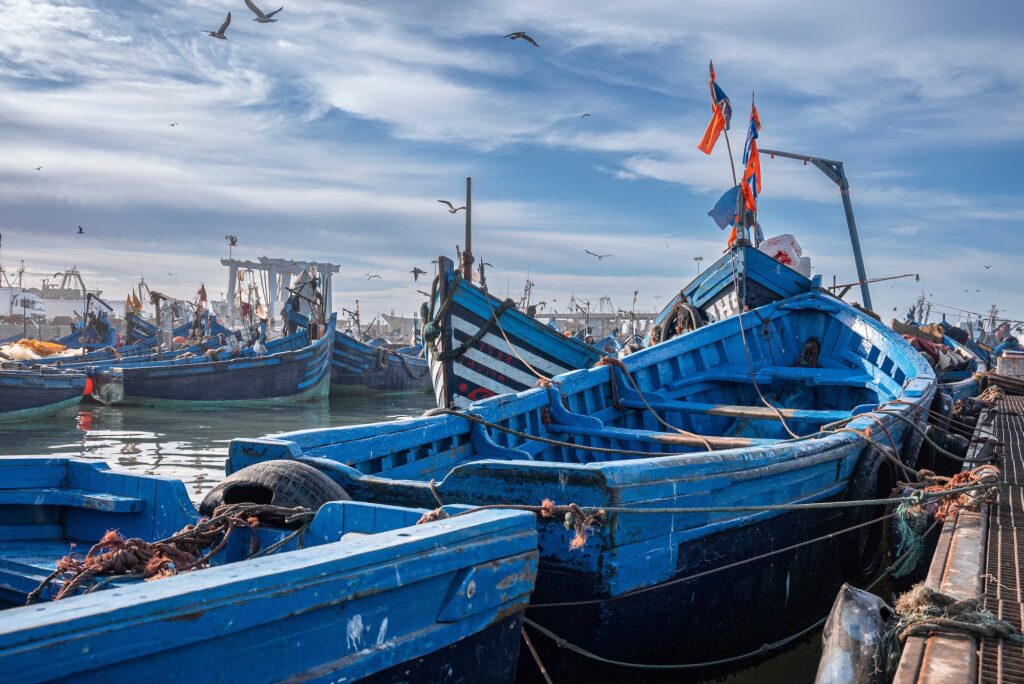 Small fishing boats moored on coast at port against cloudy sky Wooden fishing boats moored in harbor