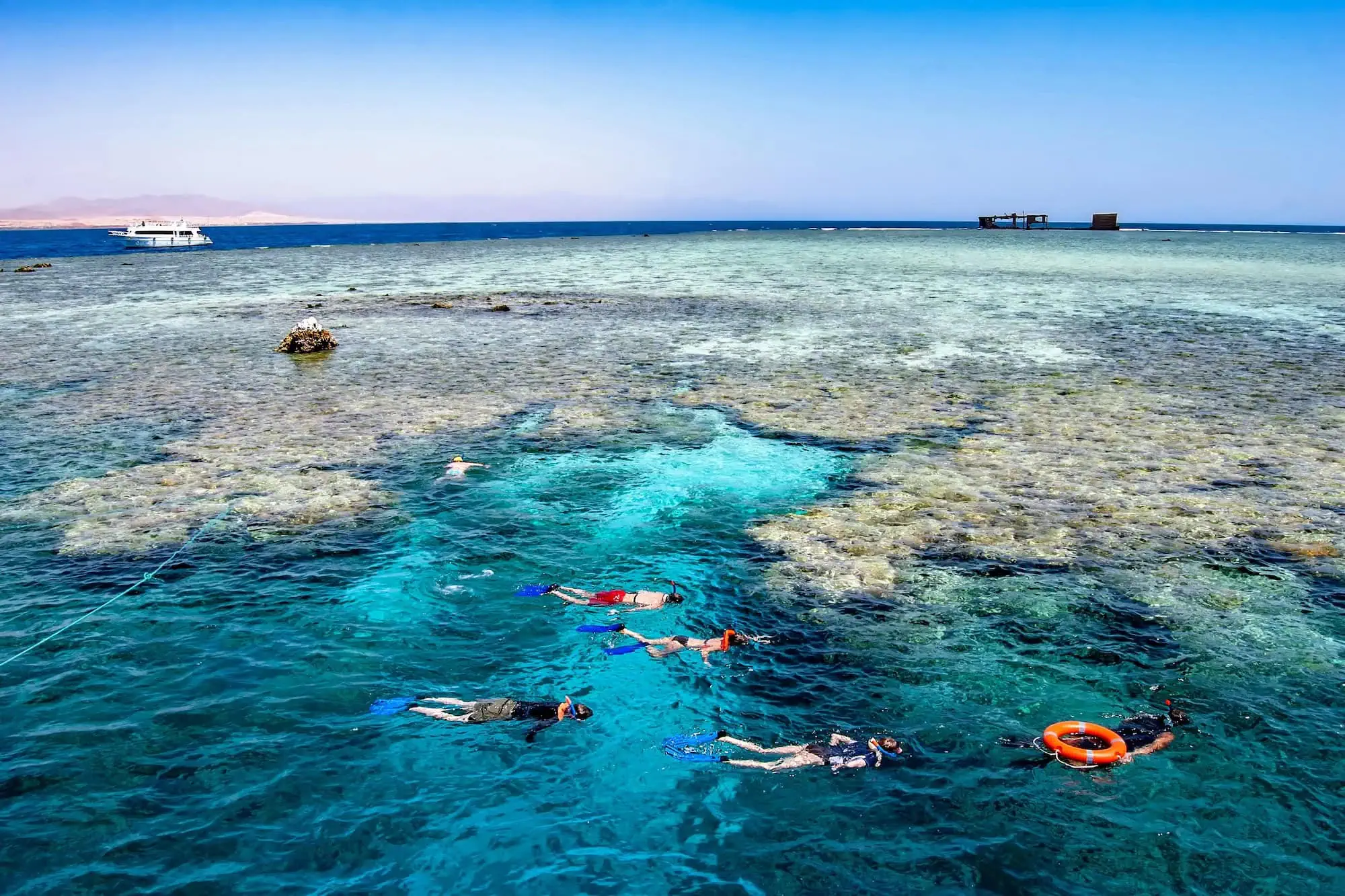 Snorkelers exploring vibrant coral reef in Red Sea with boat and safety equipment