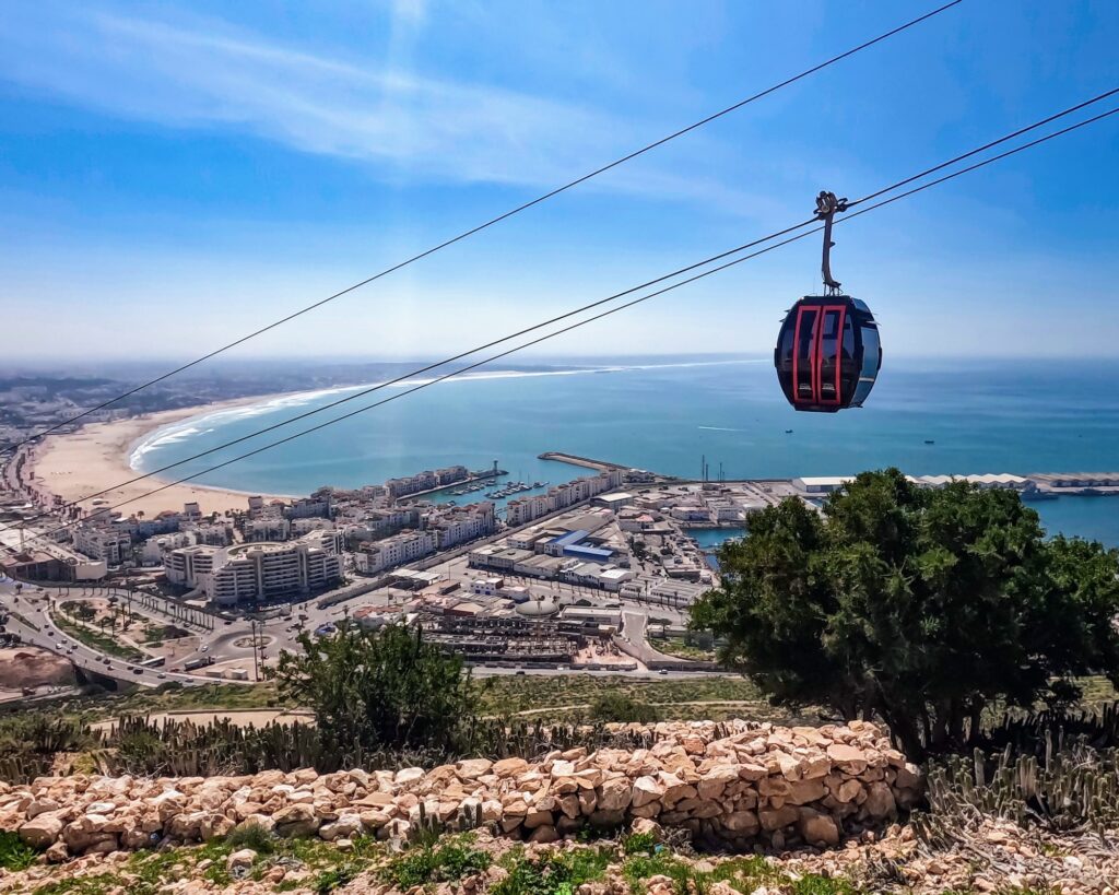 Midway view from Agadir Oufla climb, capturing Agadir's cityscape, Atlantic beach and cable cars under the sunny sky