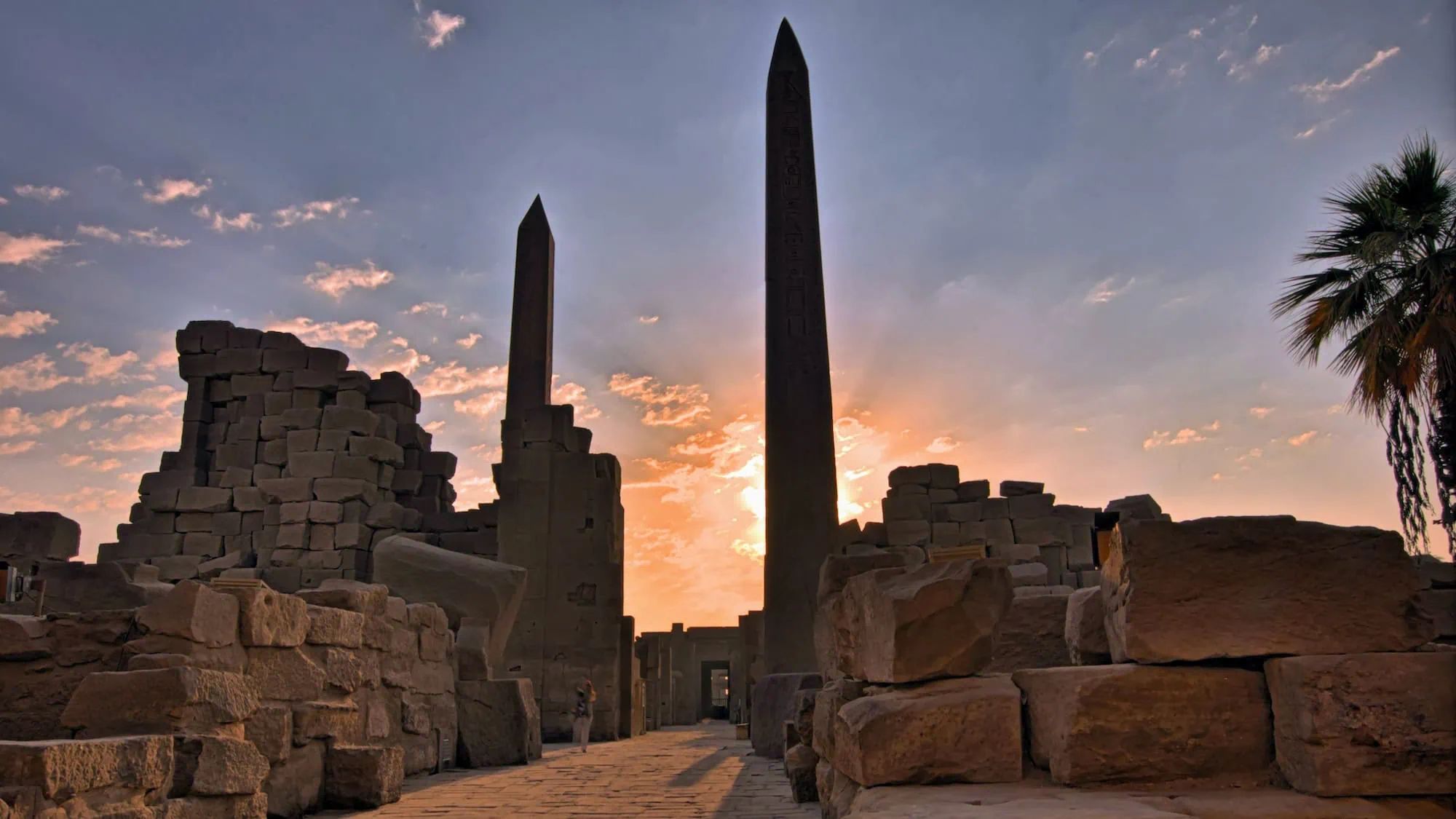Ancient Karnak Temple complex at sunrise with two tall obelisks rising from sandstone ruins
