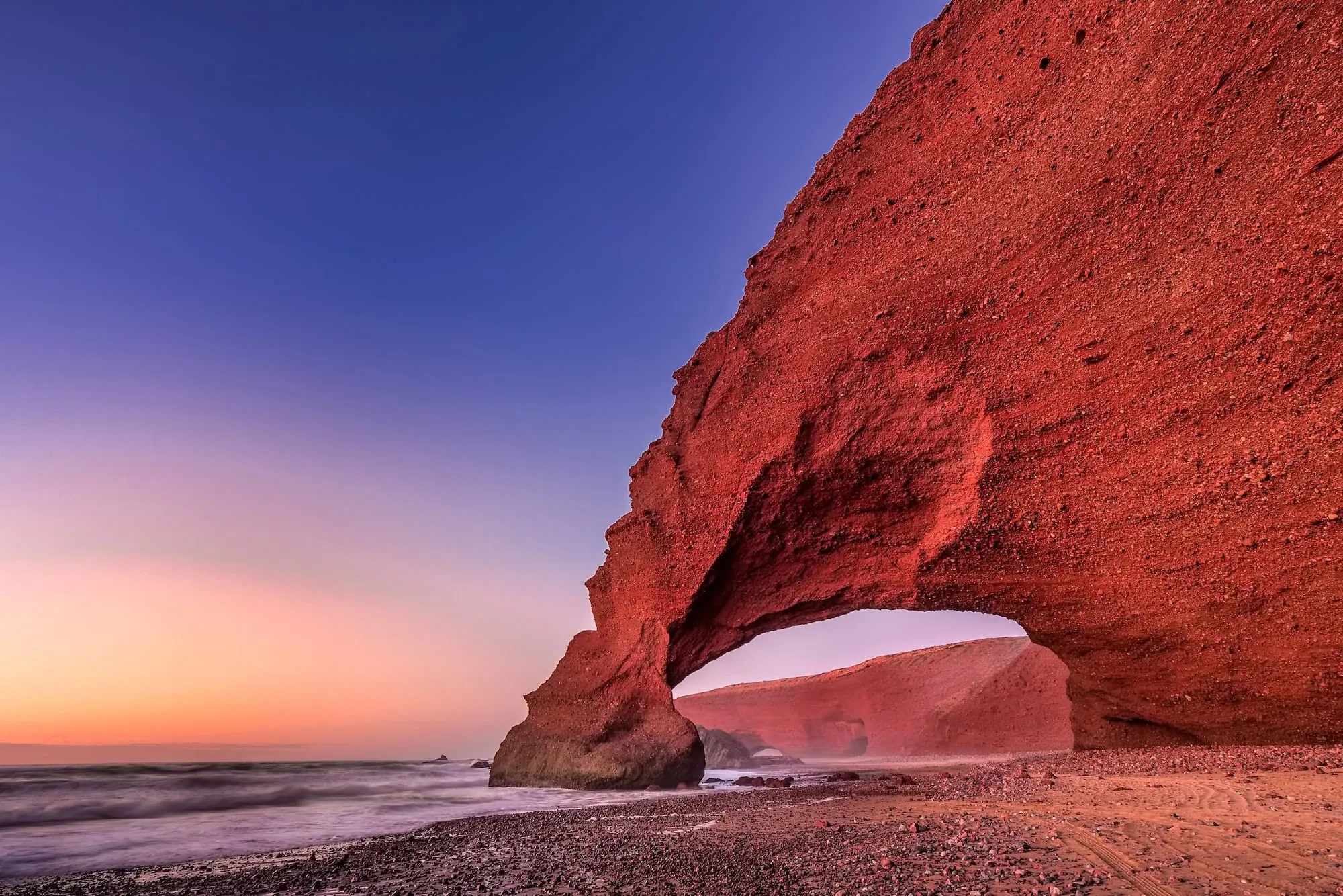 Natural red sandstone arch at Legzira Beach during sunset with dramatic coastal cliffs