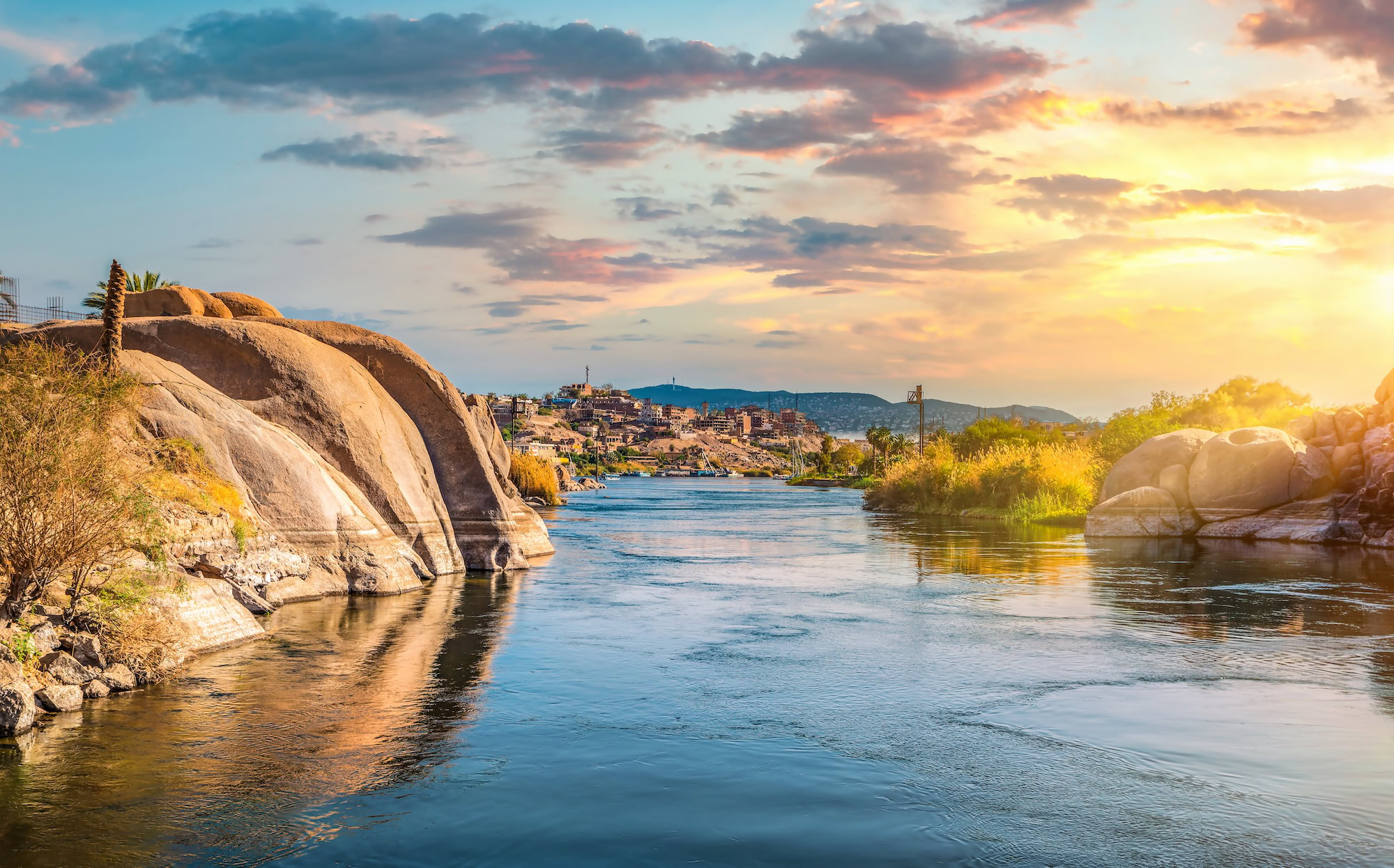 Traditional boats on the Nile River during golden hour sunset with granite rocks