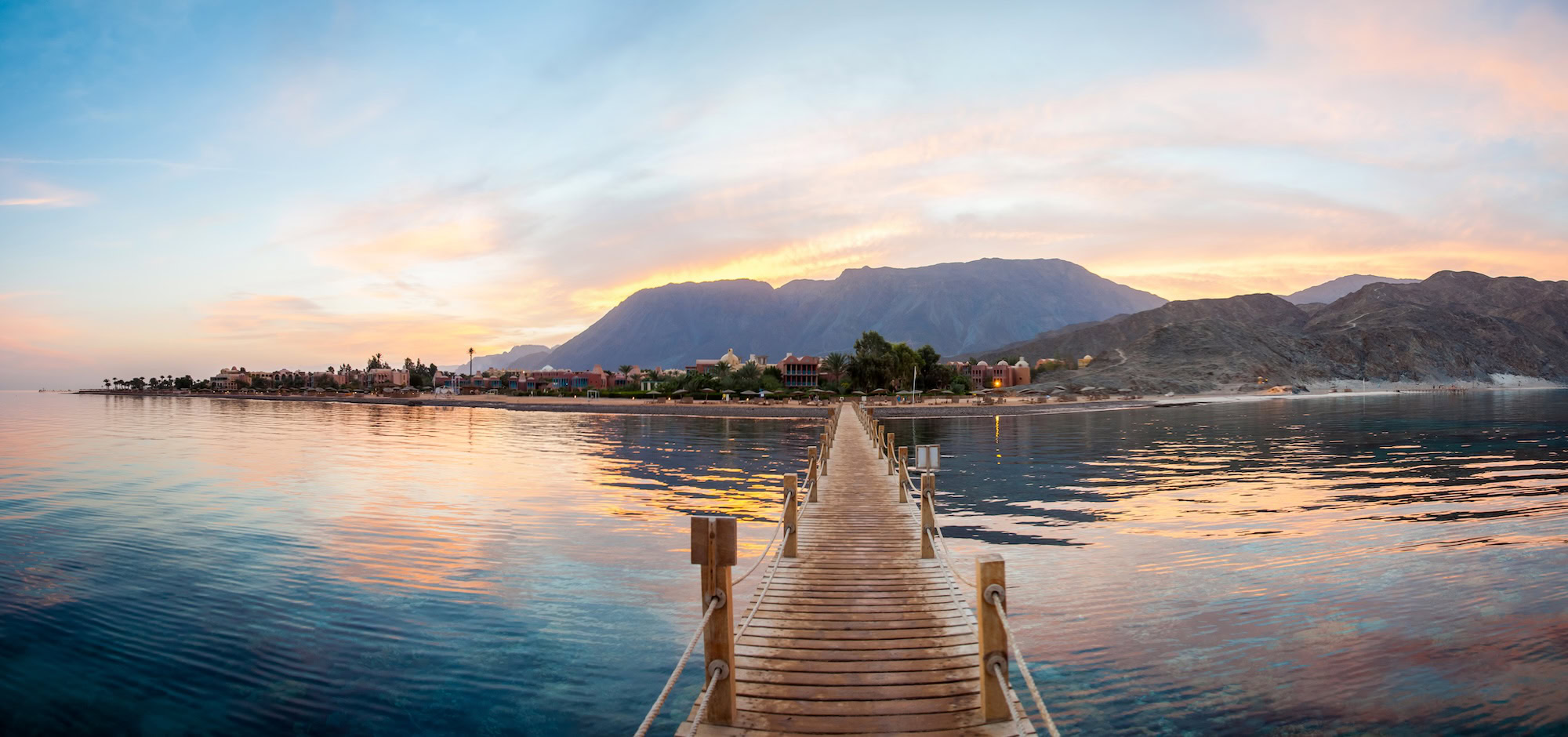 Wooden pier extending into Red Sea with coastal buildings and mountains in Dahab, Egypt