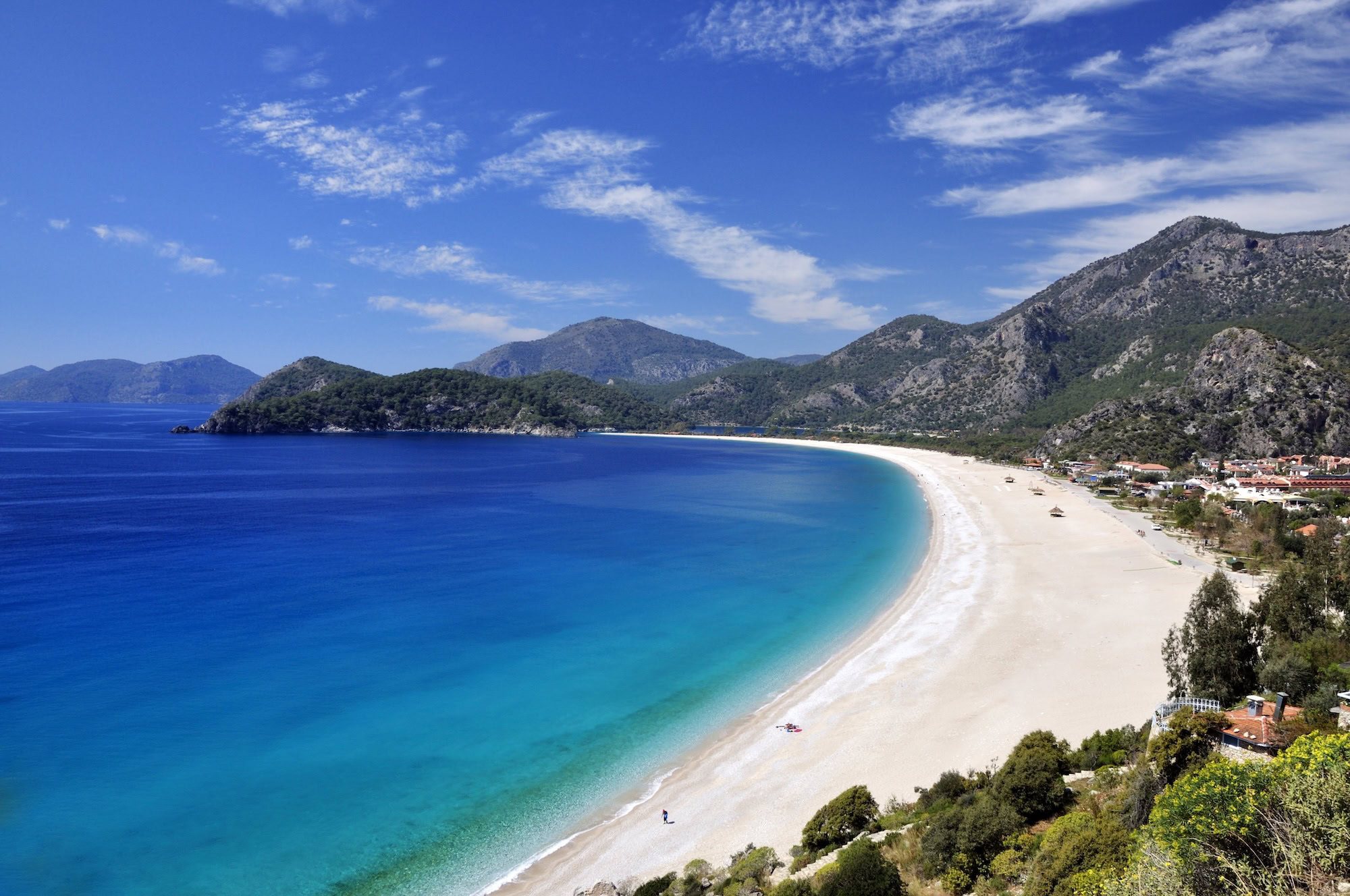 Baia a mezzaluna con spiaggia dorata e mare turchese circondata da montagne