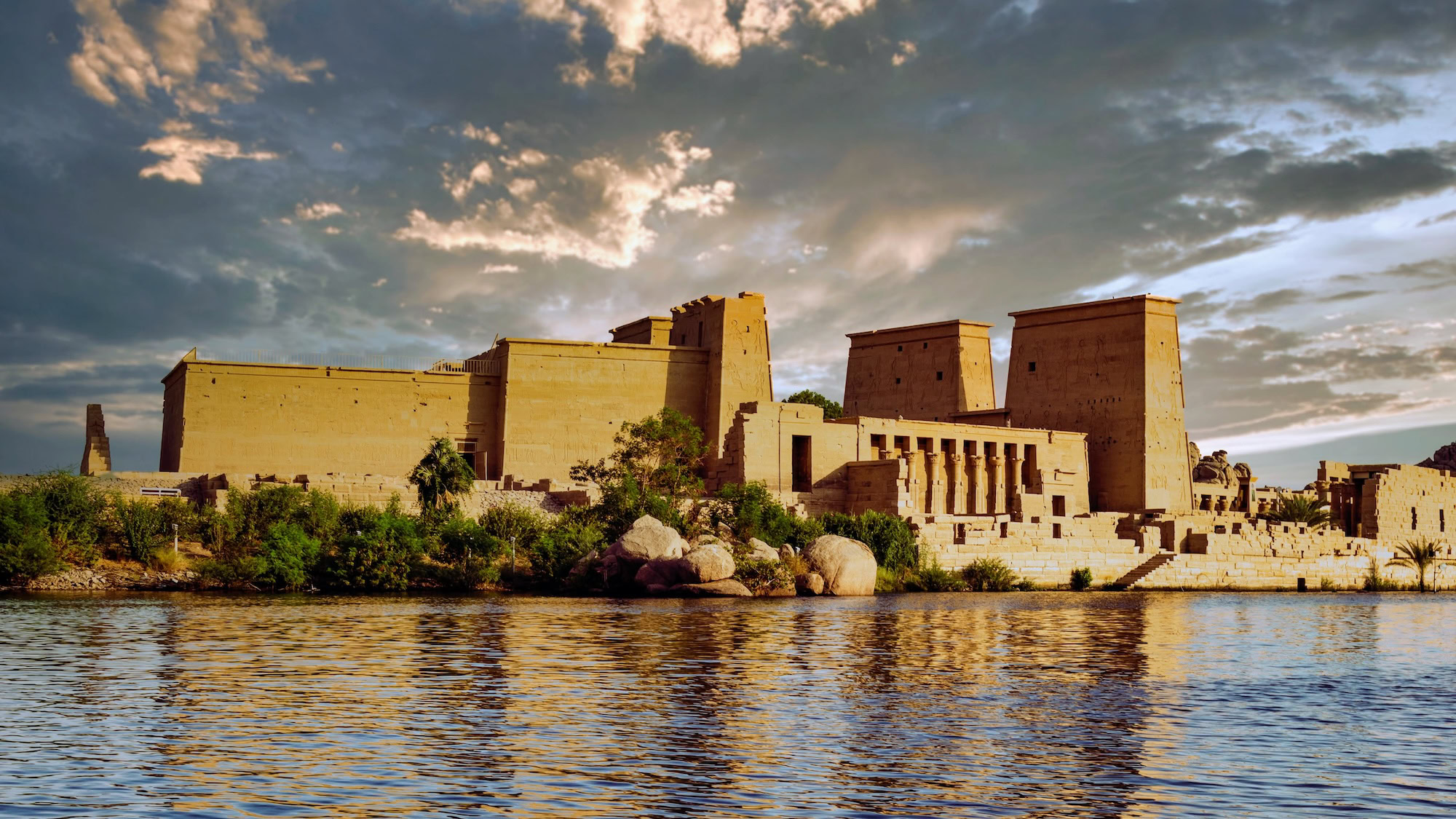 Ancient Philae Temple columns reflected in peaceful Nile waters with palm trees