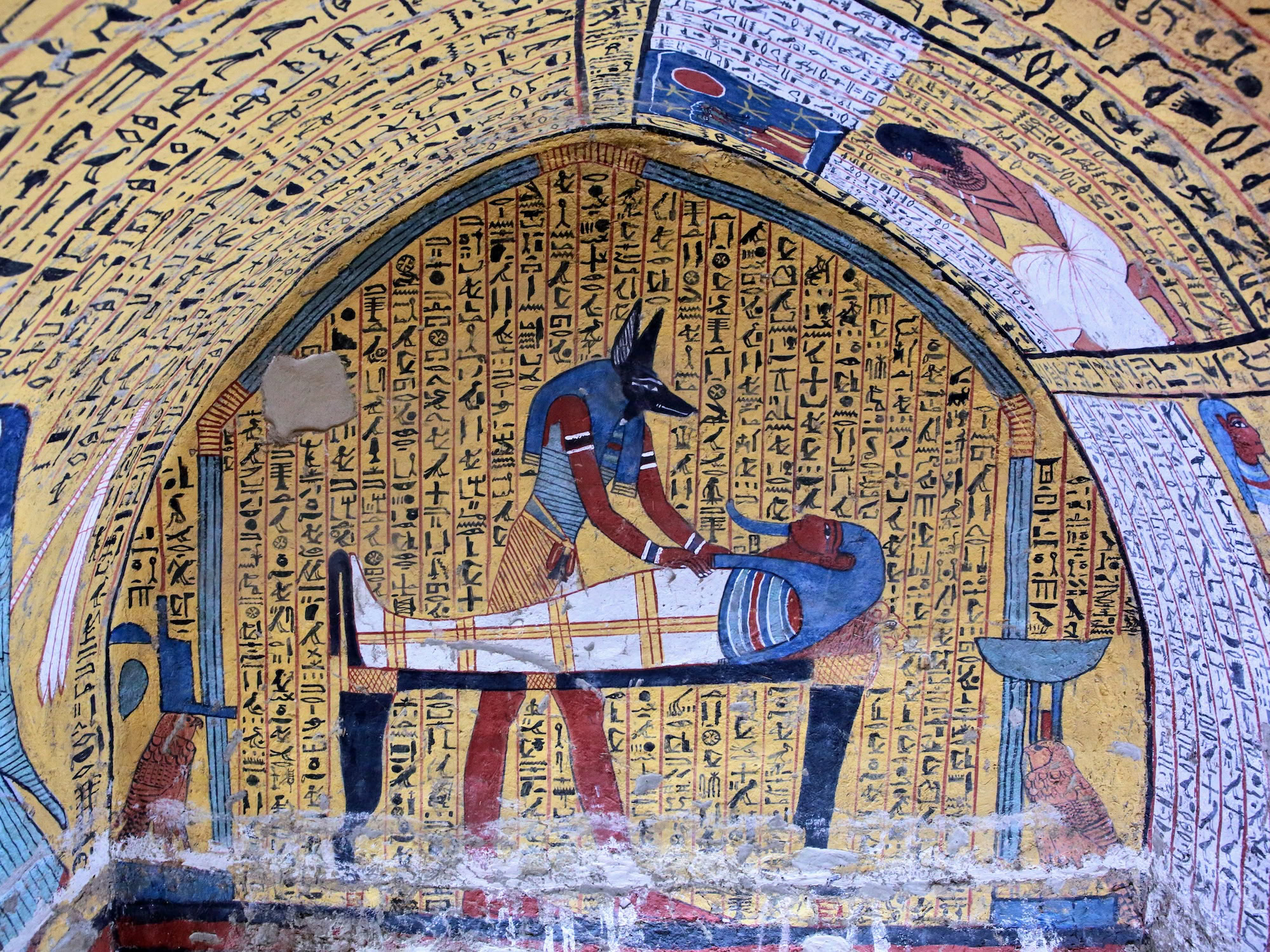 Ancient Egyptian tomb wall painting depicting Anubis, mummy, and sarcophagus with hieroglyphics