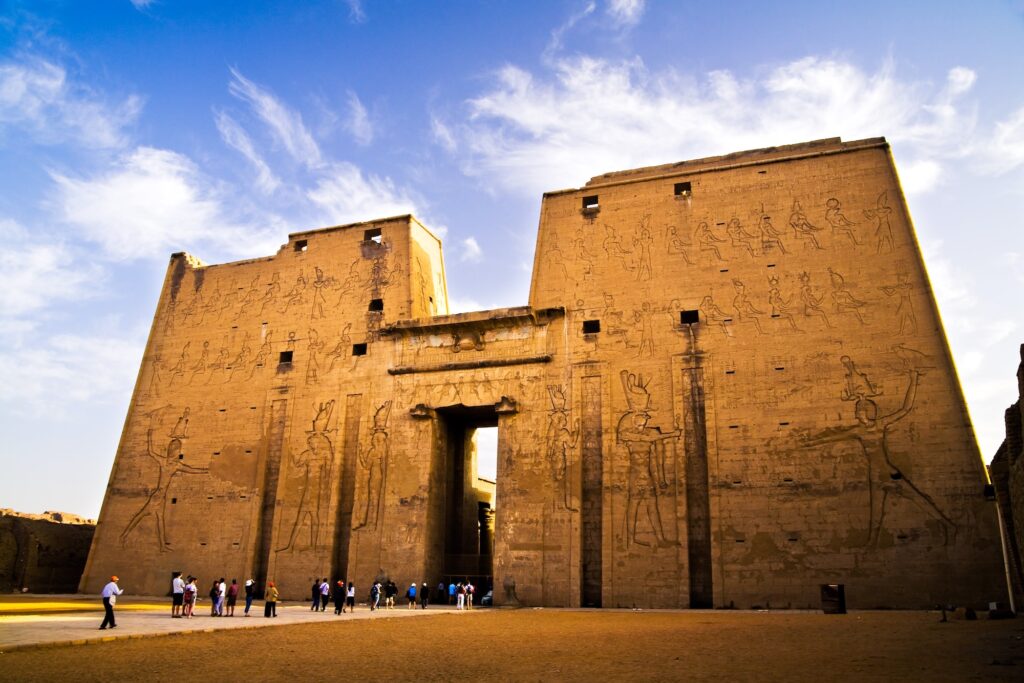 The 36-metre first pylon of the Temple of Horus at Edfu, with relief carvings and visitors at the base for scale, Egypt.