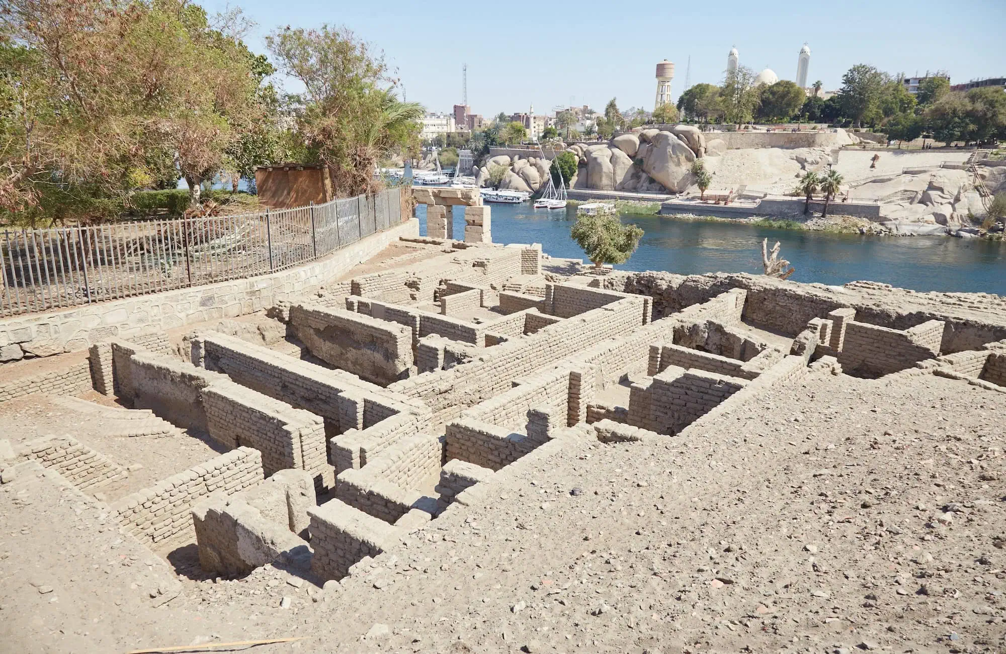 Ancient brick ruins on Elephantine Island with river, boats, and modern buildings in background