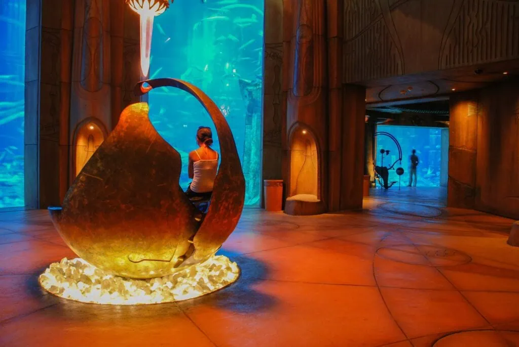 Visitor seated inside a shell-shaped installation overlooking aquarium tanks at The Lost Chambers Aquarium