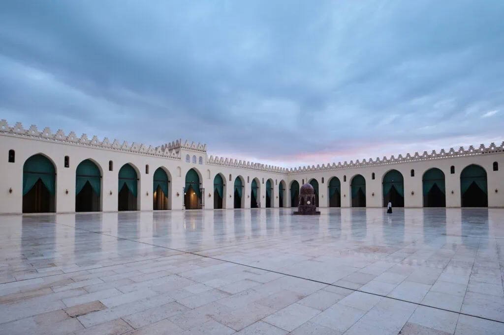 An interior view with white marble flooring, stone arcades, and open courtyard space inside the Al-Hakim Mosque, Cairo