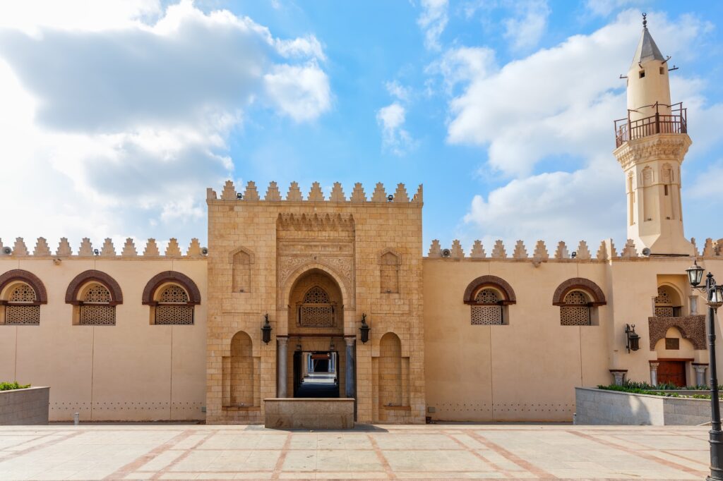 An exterior view of the main entrance facade with stone portal, crenellated walls, and minaret at the Mosque of Amr ibn al-As, Old Cairo, Cairo