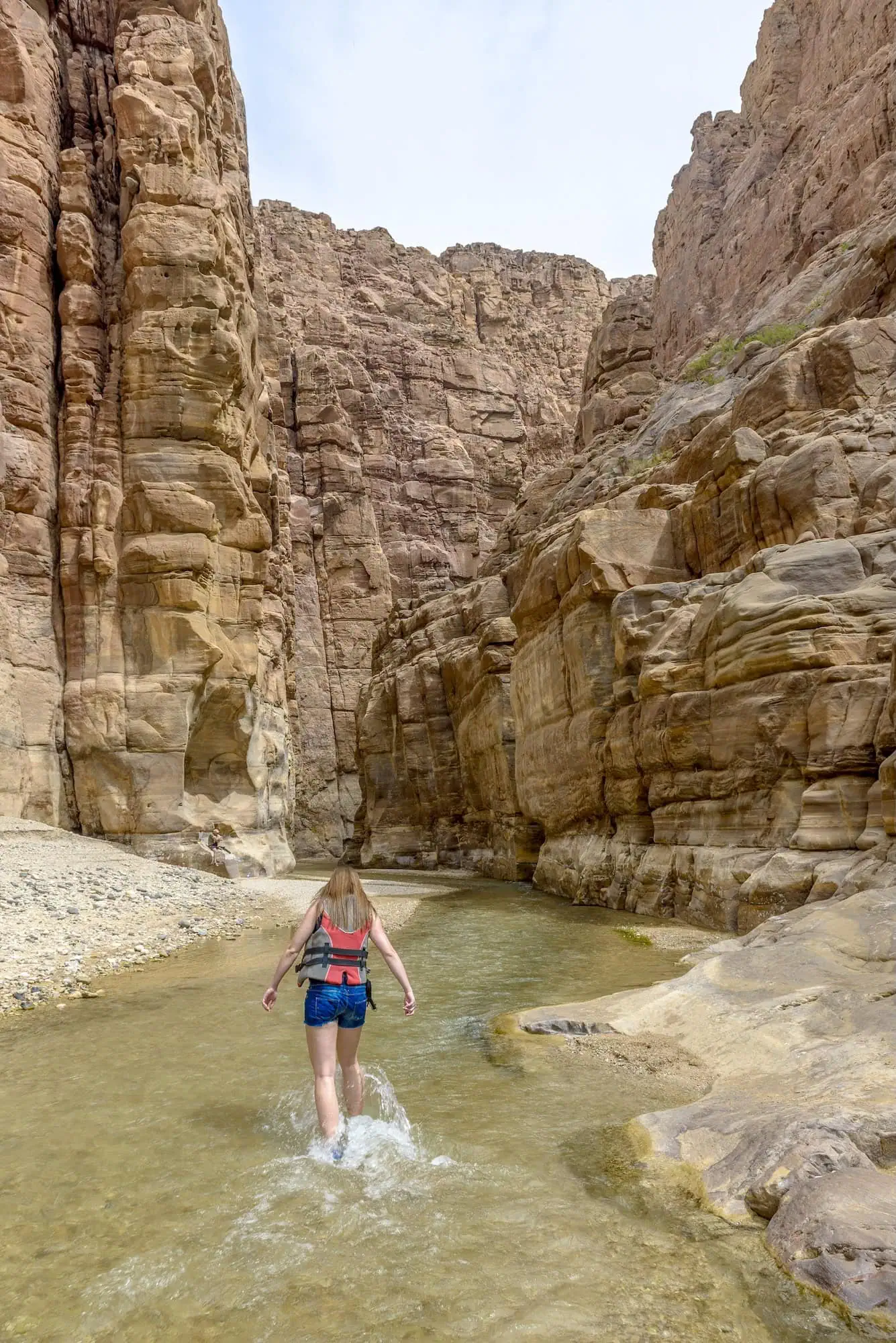 Person wading through water in narrow Wadi Mujib canyon with towering sandstone cliffs