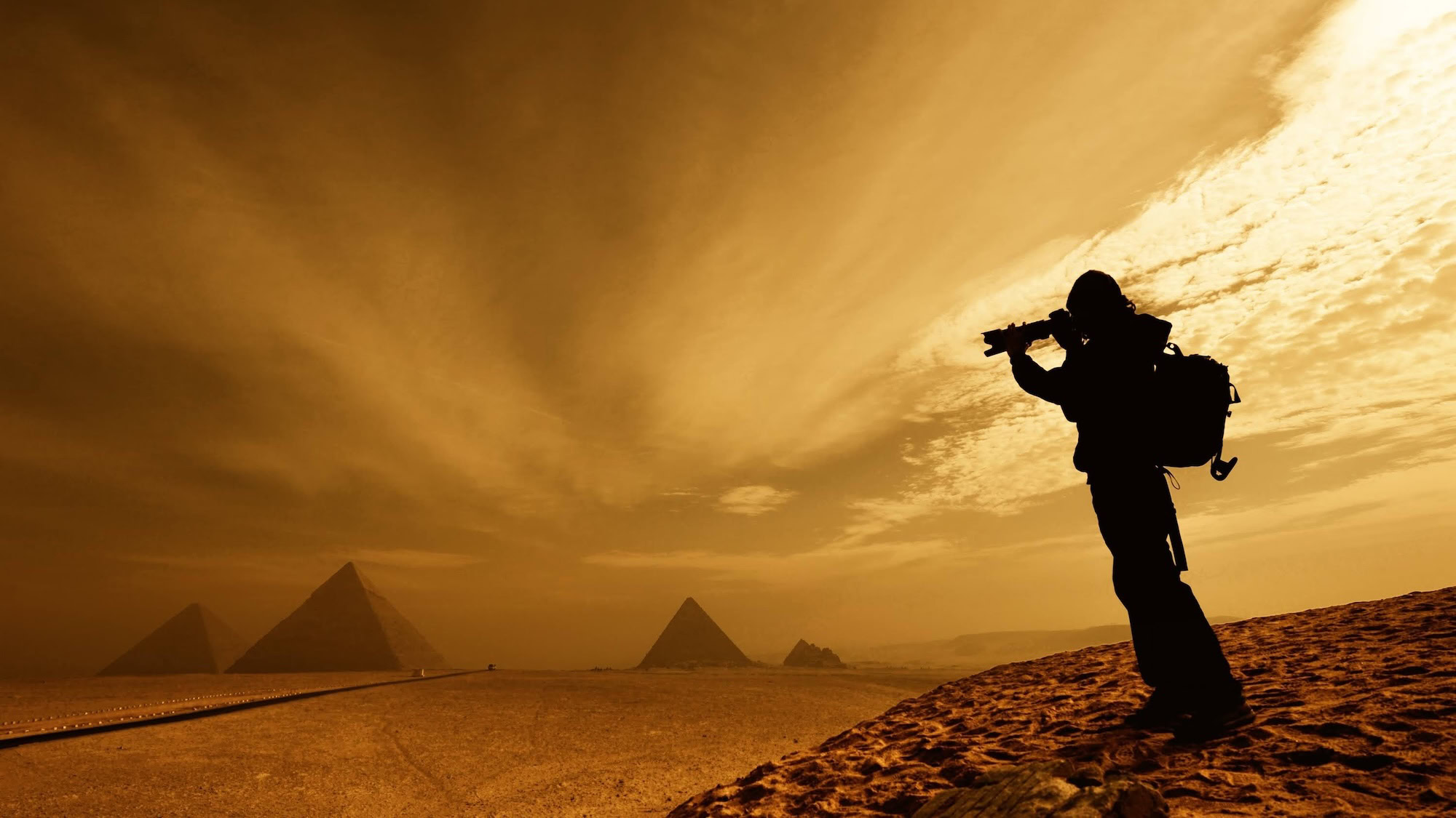 Photographer with camera capturing silhouette of pyramids in desert landscape