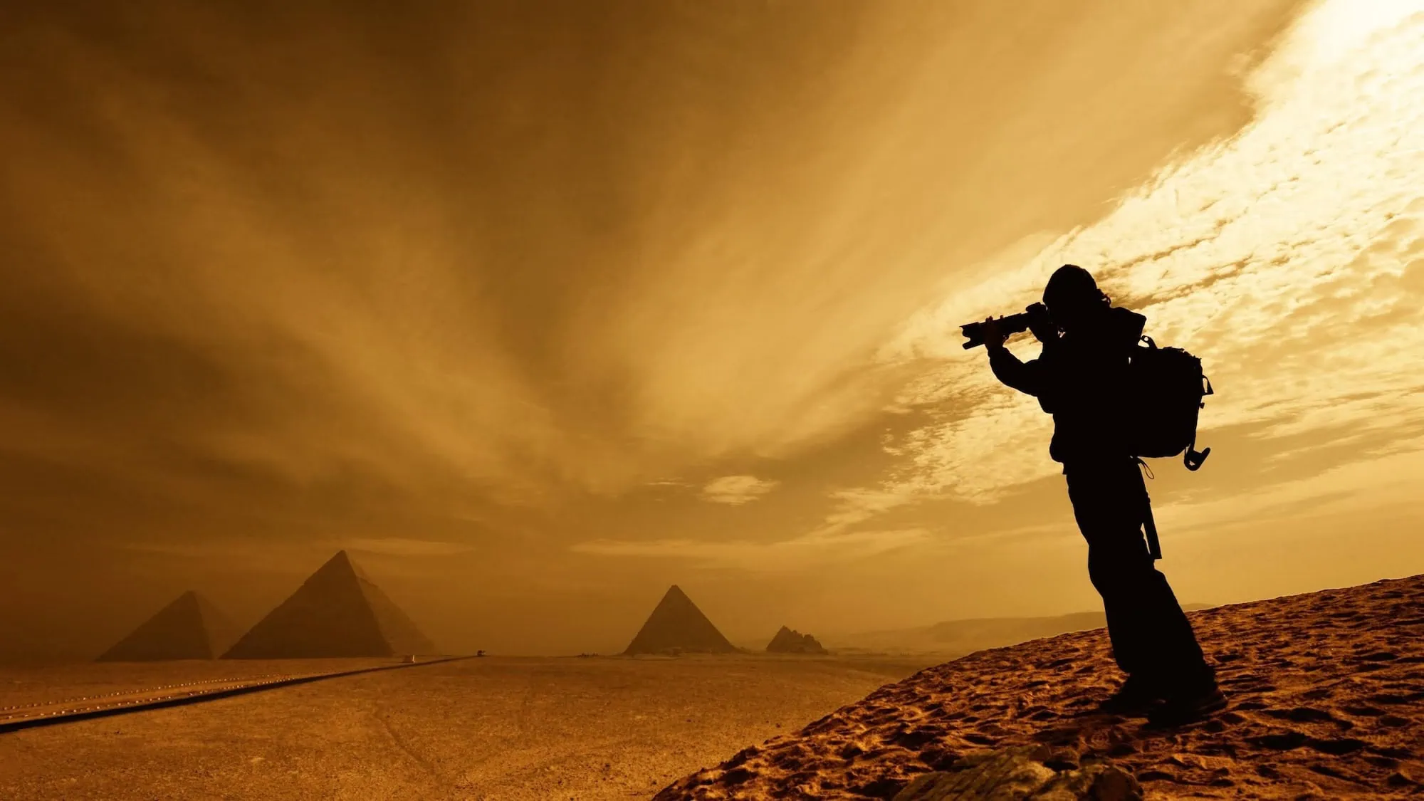 Photographer with camera capturing silhouette of pyramids in desert landscape