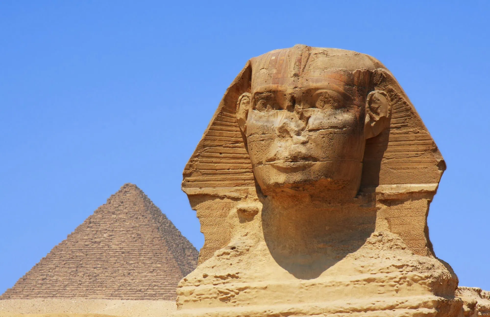 The Great Sphinx of Giza with a pyramid behind it under a clear blue sky on the Giza plateau outside Cairo.