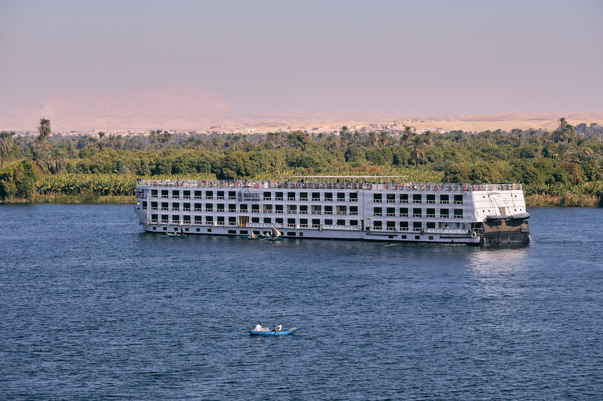Nile River cruise ship sailing past palm trees and desert landscape in Egypt