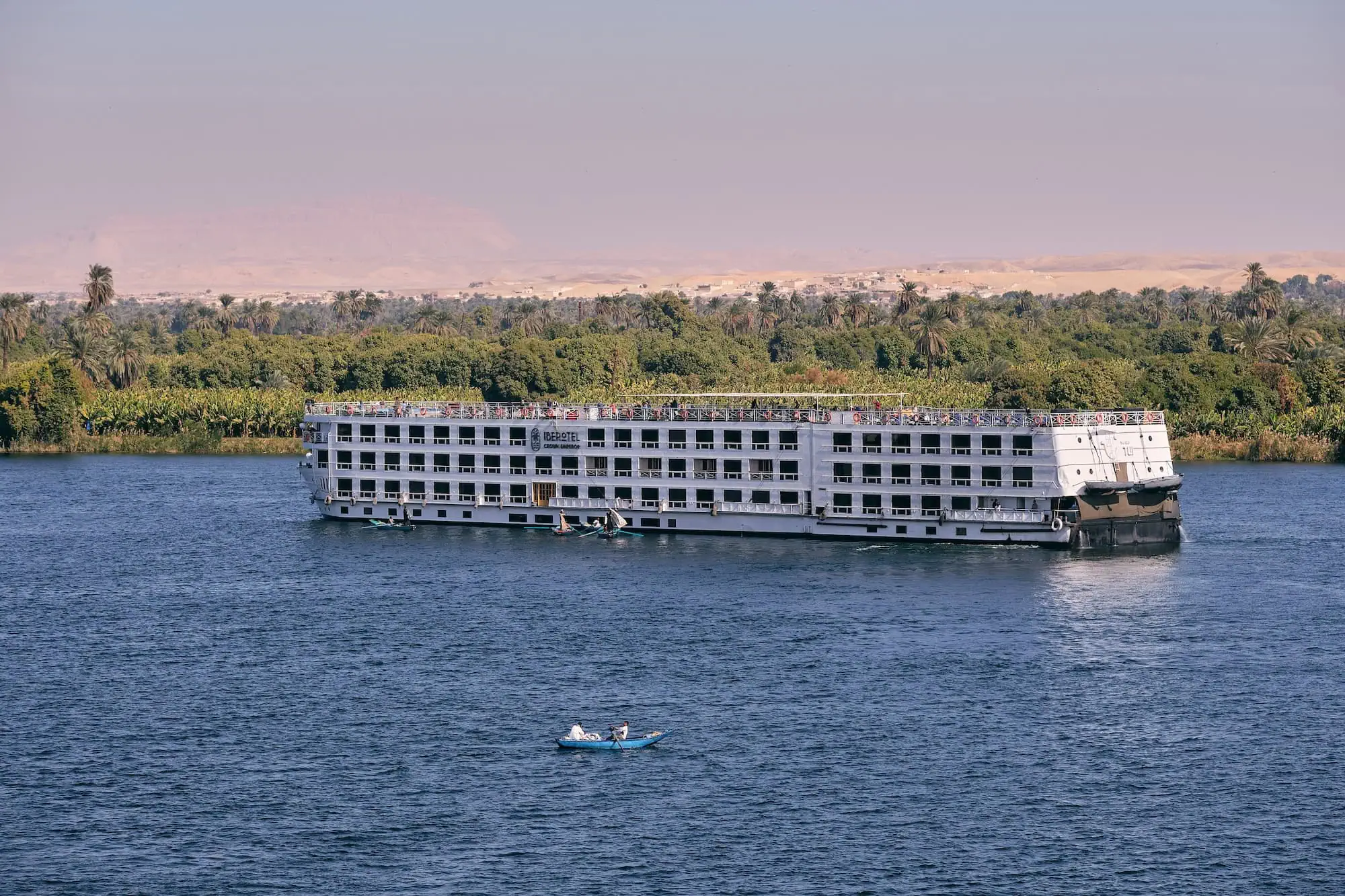 Nile River cruise ship sailing past palm trees and desert landscape in Egypt