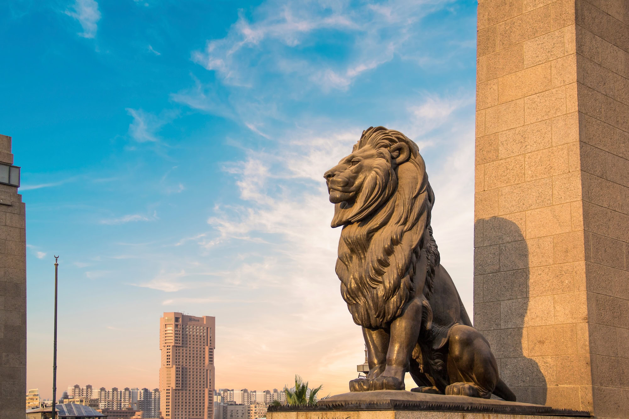 Lion statue at Qasr Al Nile Bridge with modern Cairo buildings in background