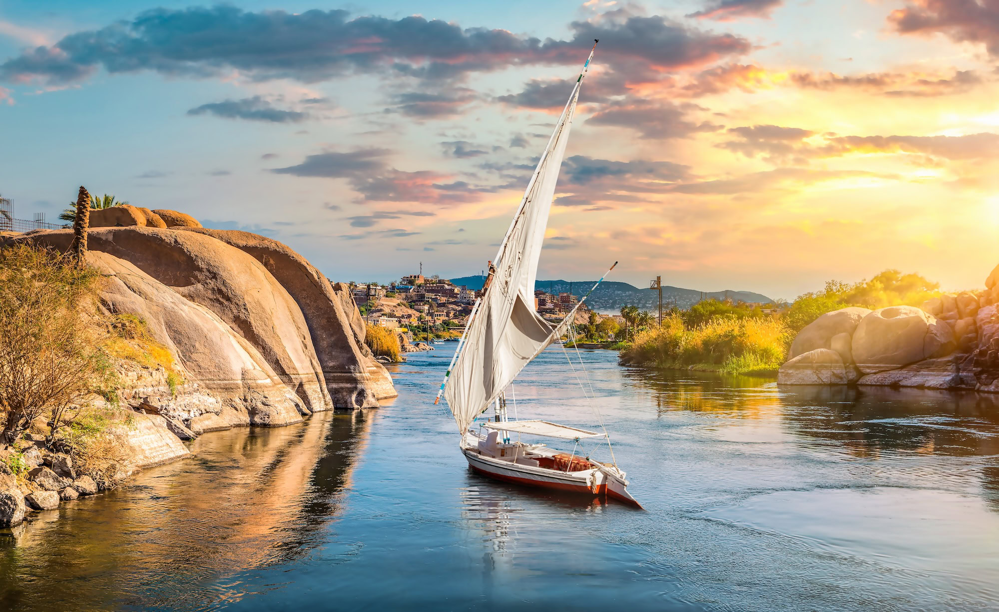 Traditional felucca sailboat on Nile River with desert landscape and sunset backdrop