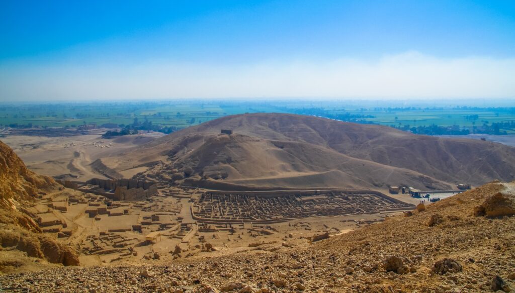 View of stone house ruins and low walls from the ancient village of Deir el-Medina set against the desert landscape, Luxor