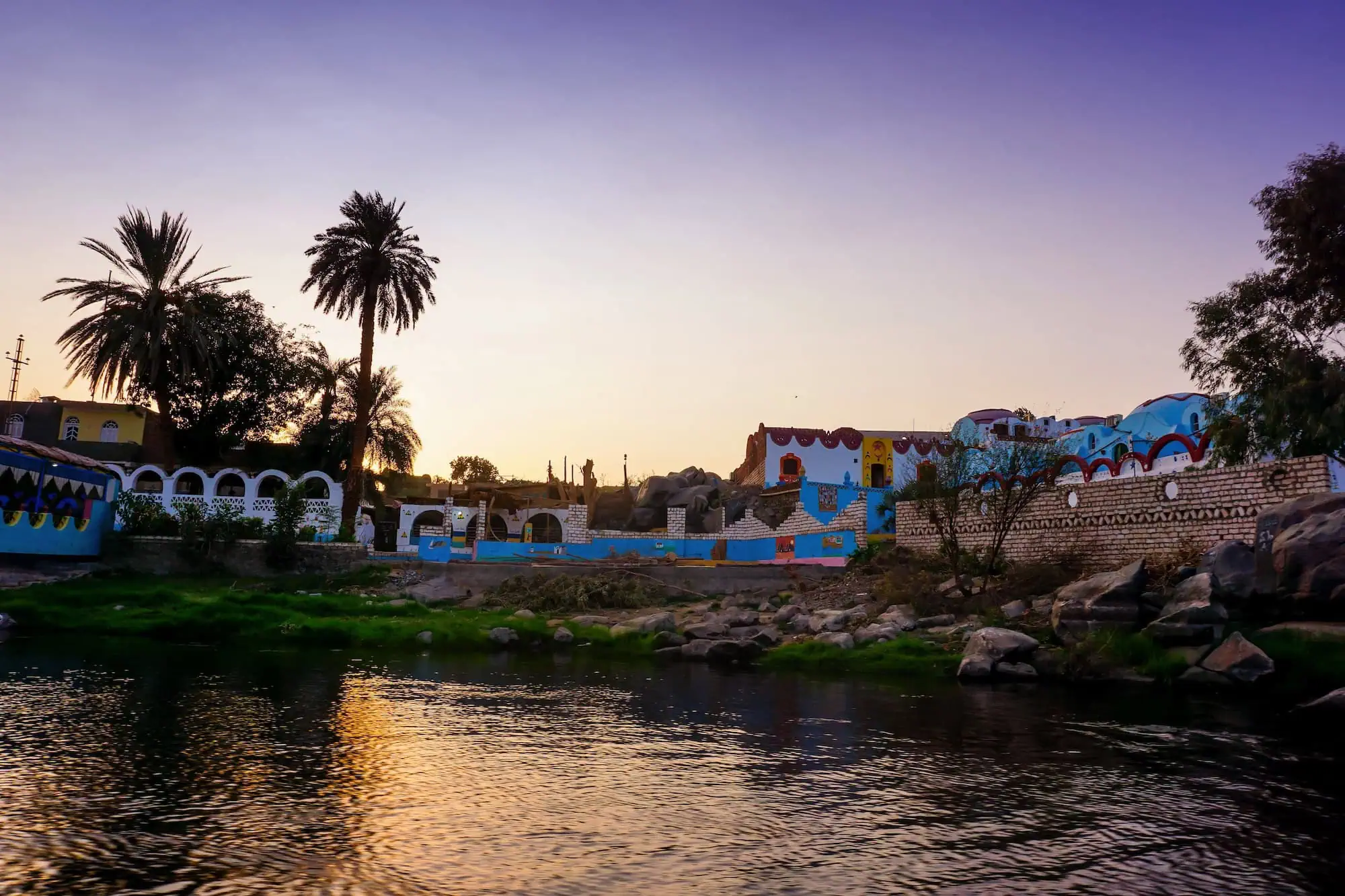 Colorful Nubian village houses along the Nile River with palm trees and traditional architecture