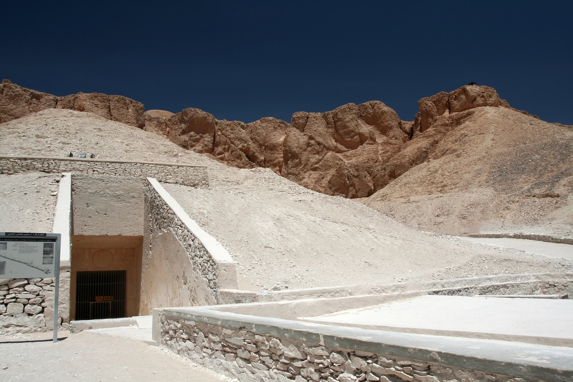 Ancient tomb entrance in Valley of the Kings with stone walls and protective barriers