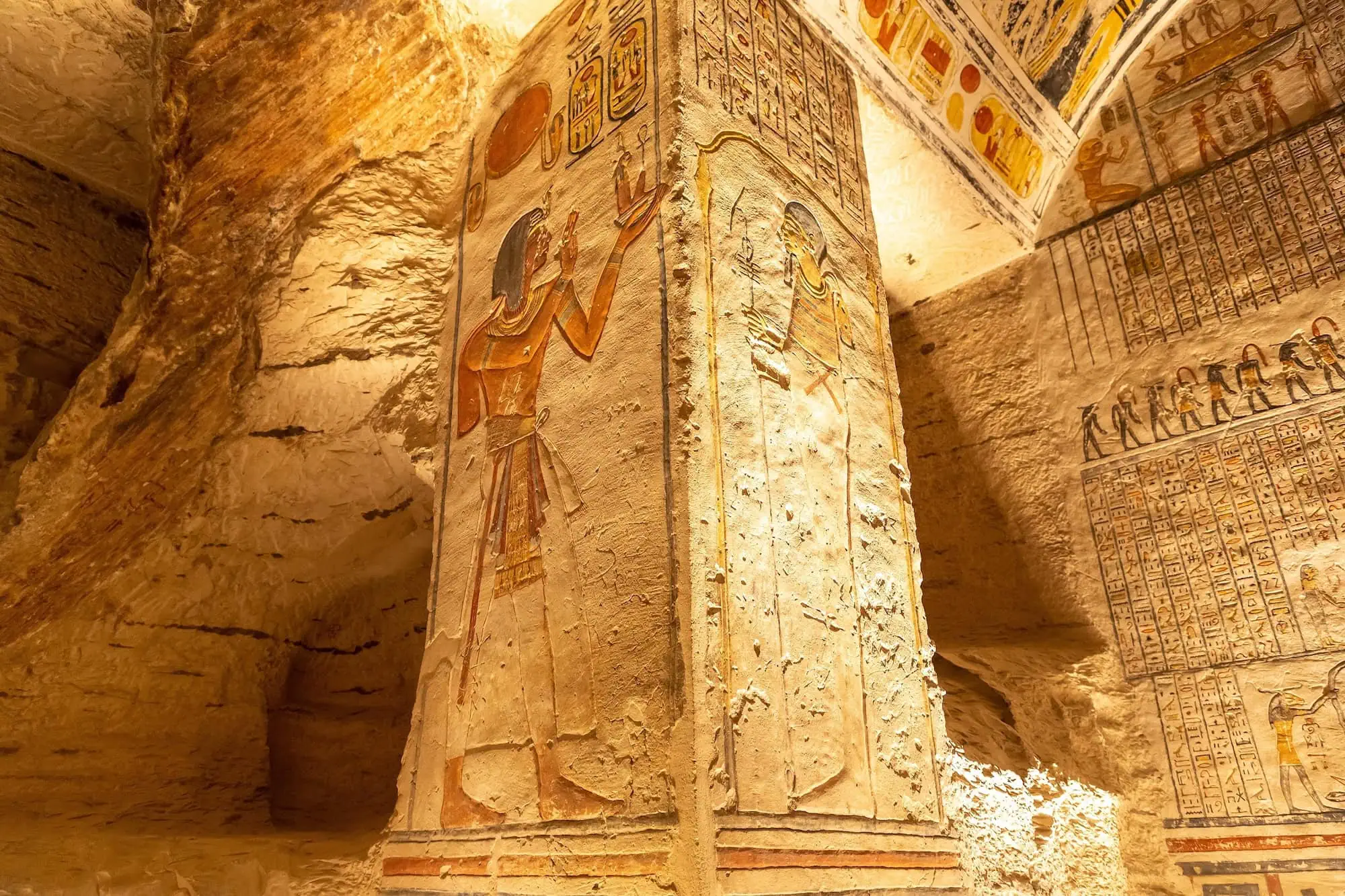 Ancient Egyptian tomb interior with colorful hieroglyphic wall paintings and carvings