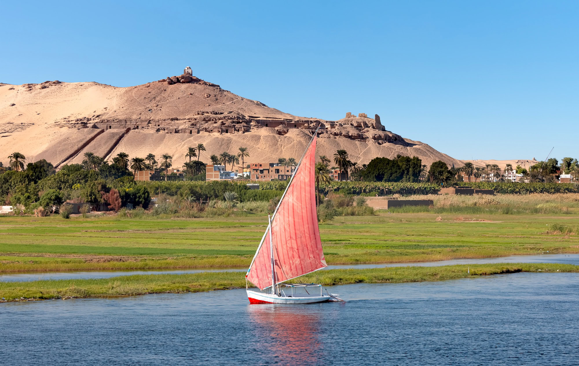 Traditional sailboat with red sail on the Nile River at sunset